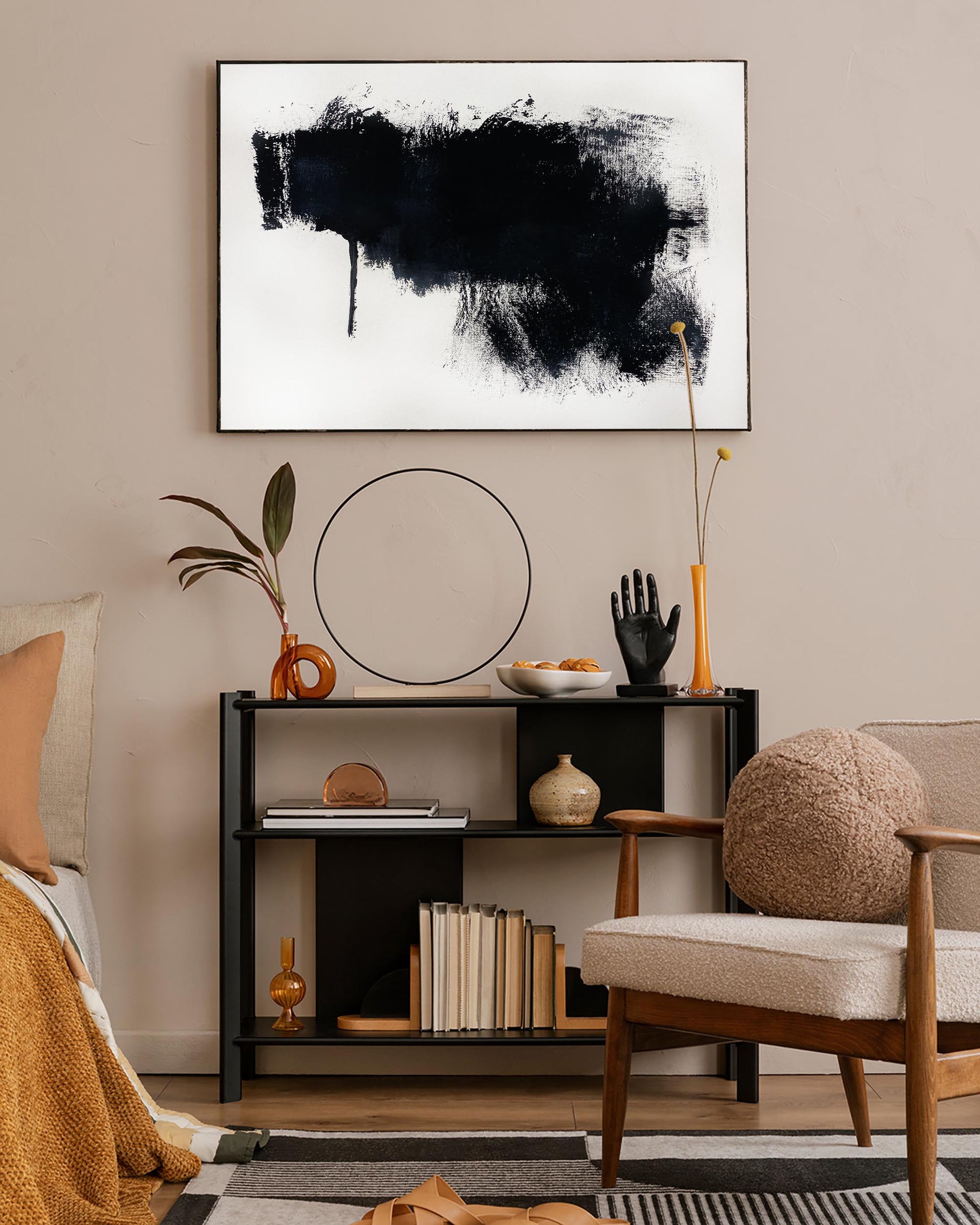 A framed canvas with an abstract black and white design hung on a wall above a console table in a living room setting.