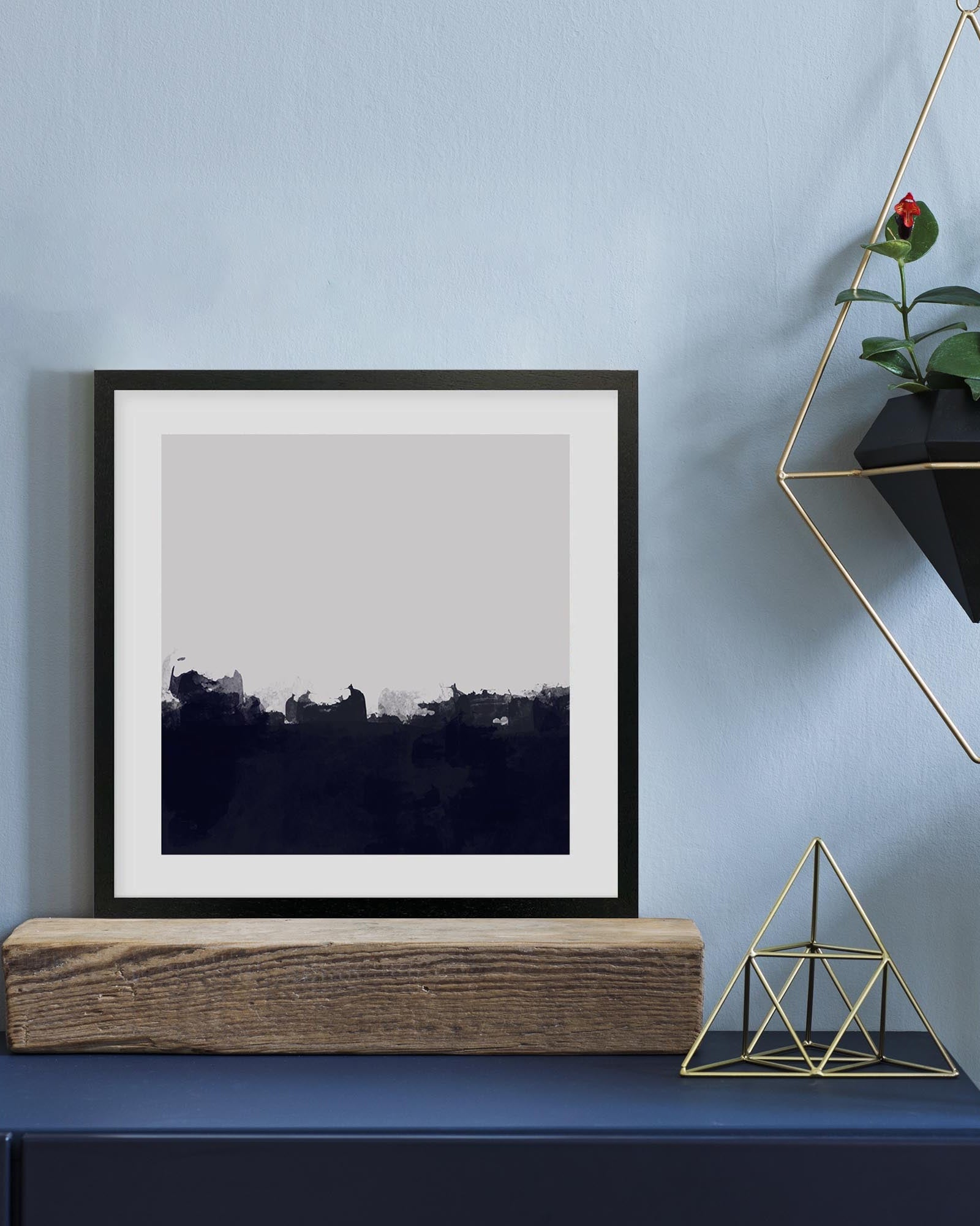 Framed artwork on a shelf with decorative items against a light blue wall