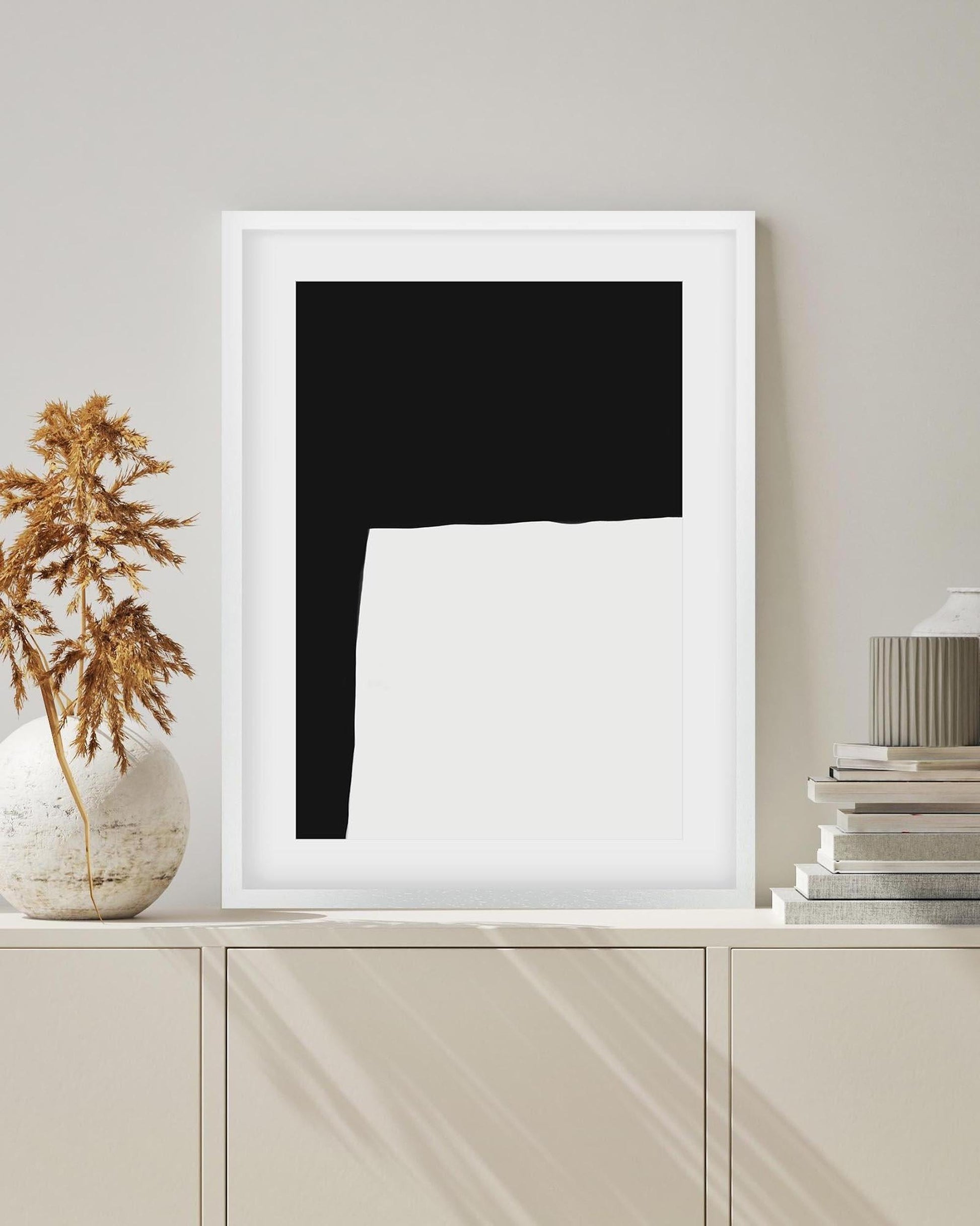 Framed abstract art piece on a white shelf with decorative items.