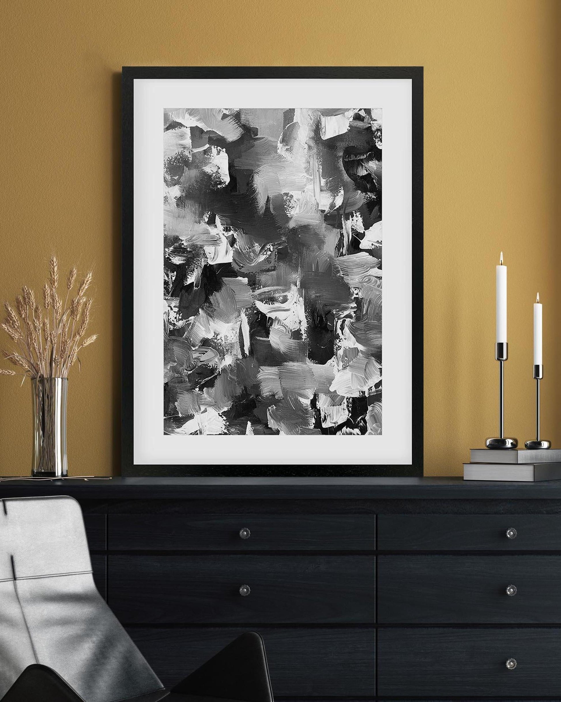 Framed abstract art print on a mustard yellow wall above a black dresser.
