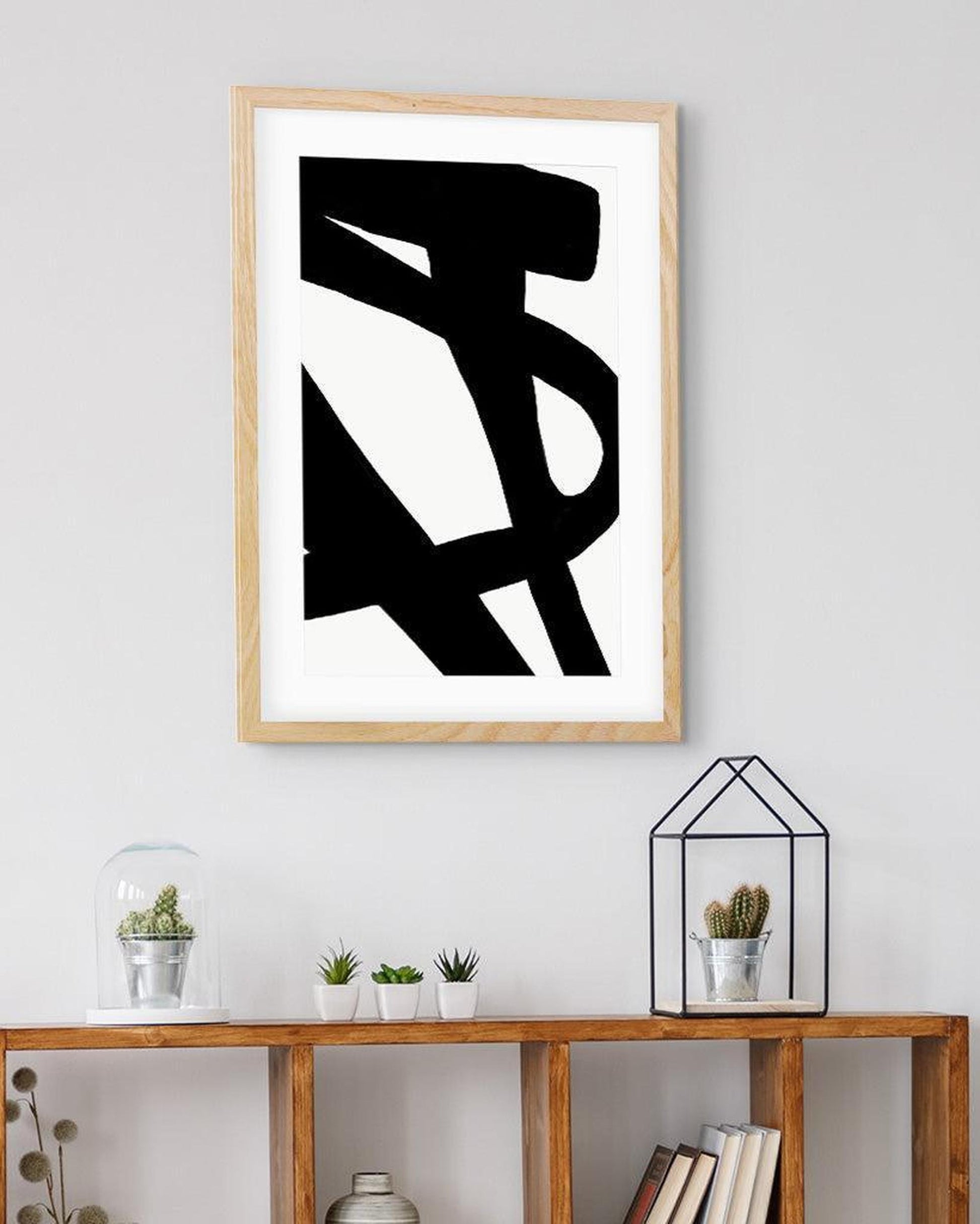 Framed abstract black and white artwork on a wall above a wooden shelf with decorative items.