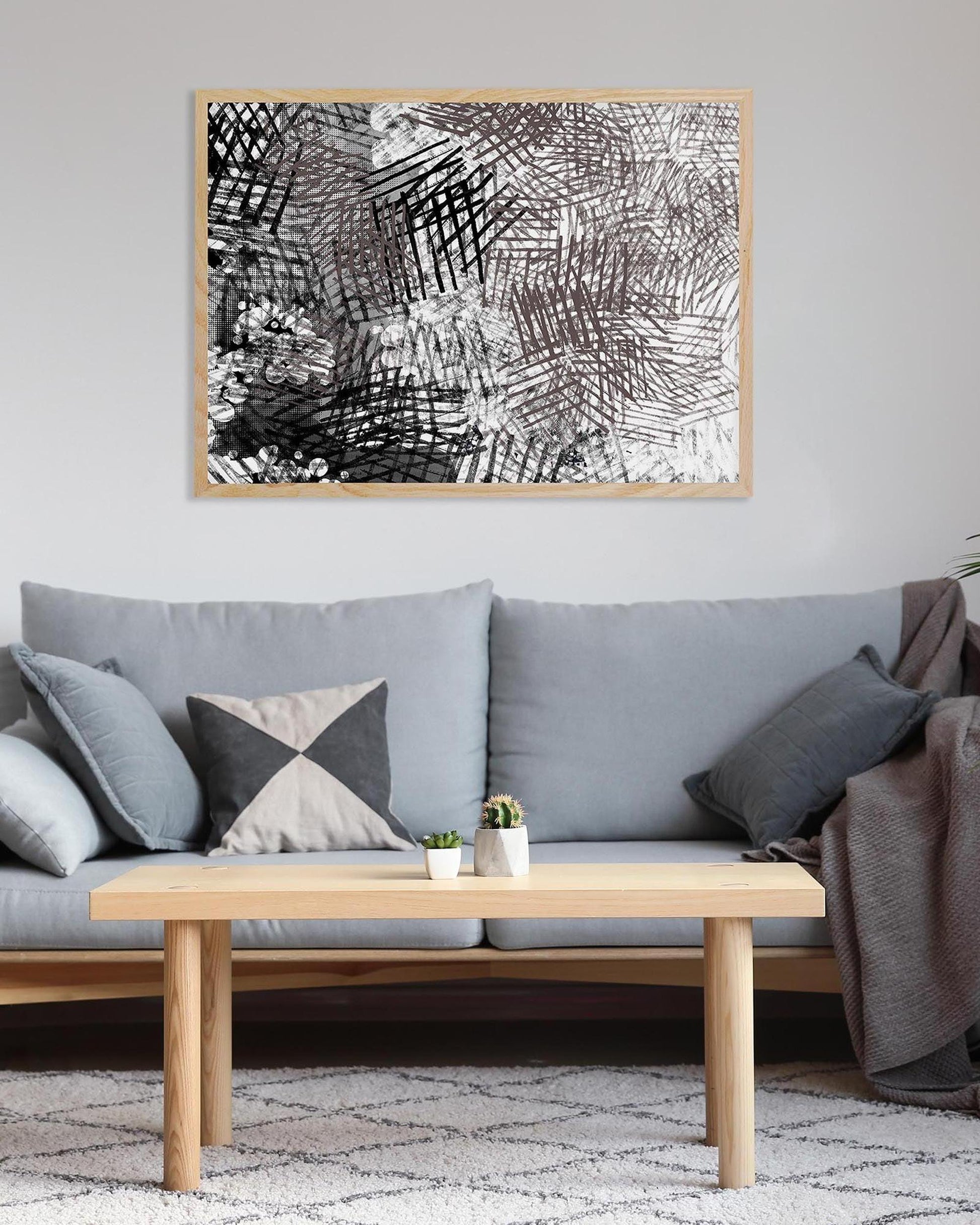 Gray sofa with decorative pillows and a wooden coffee table in a living room setting, featuring a framed abstract black and white artwork on the wall.