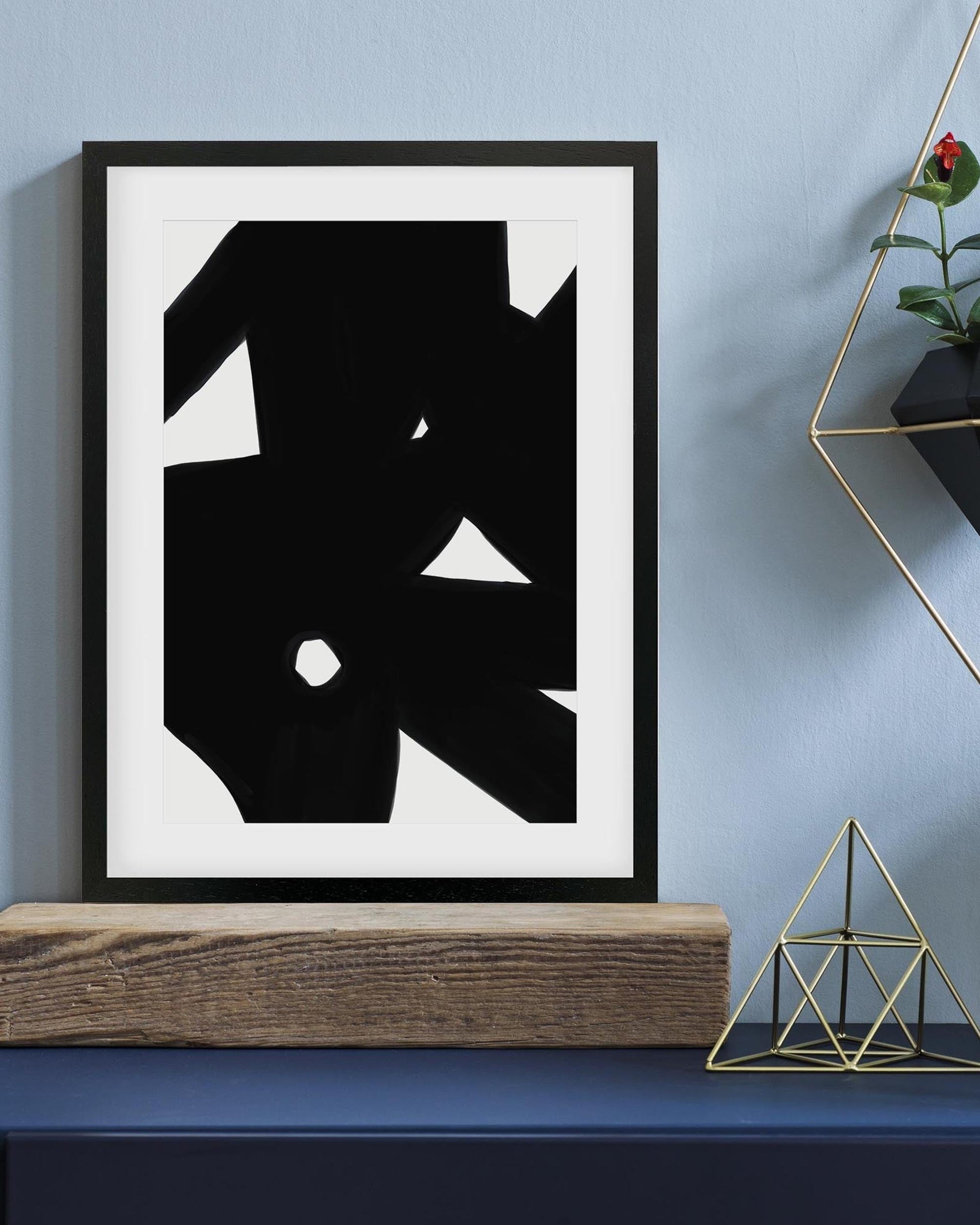 Abstract black and white artwork in a frame on a blue wall with decorative elements.