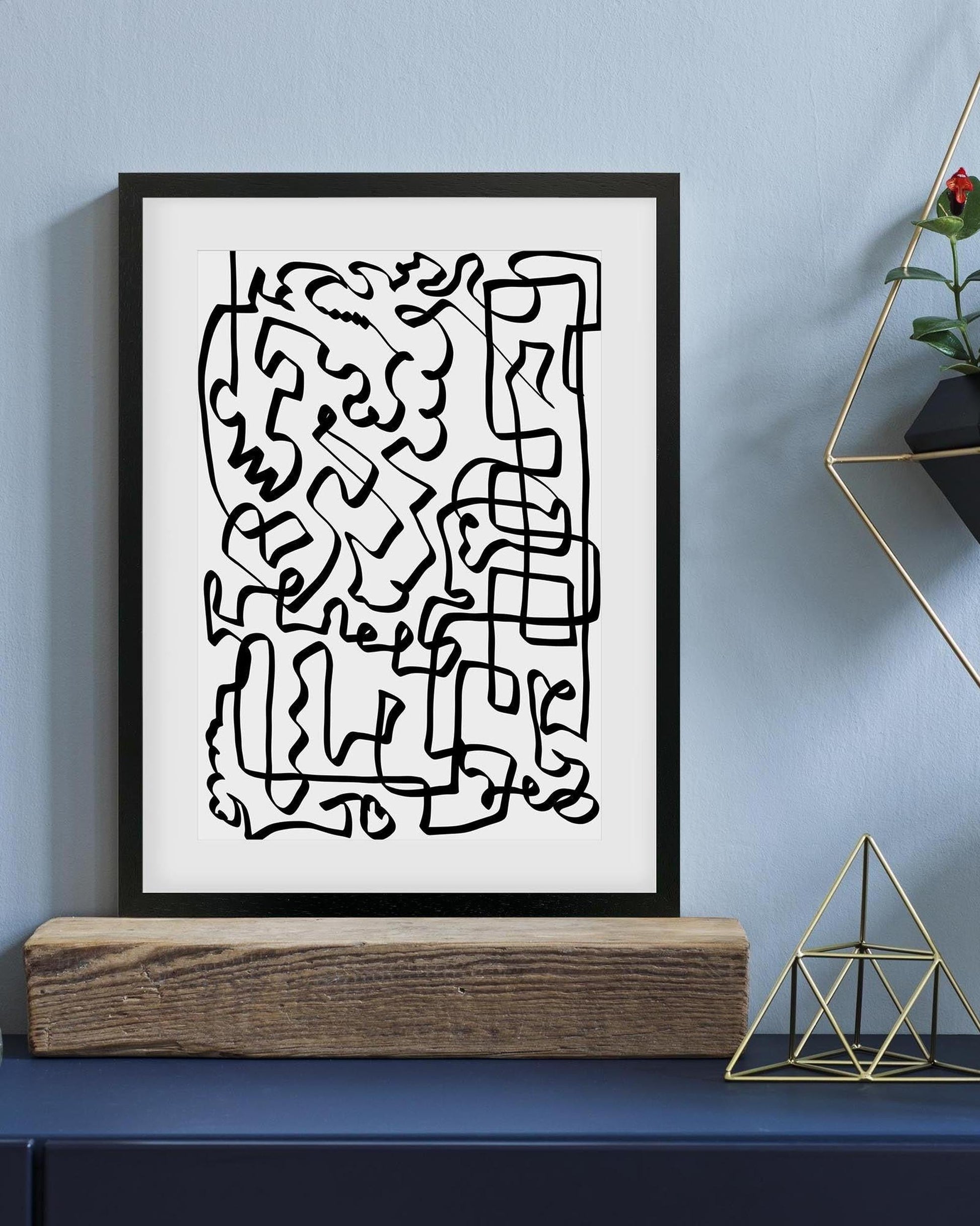 Framed abstract black line art on a white background against a blue wall.