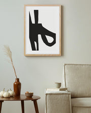 Framed abstract black and white artwork on a wall above a wooden side table with decorative items.
