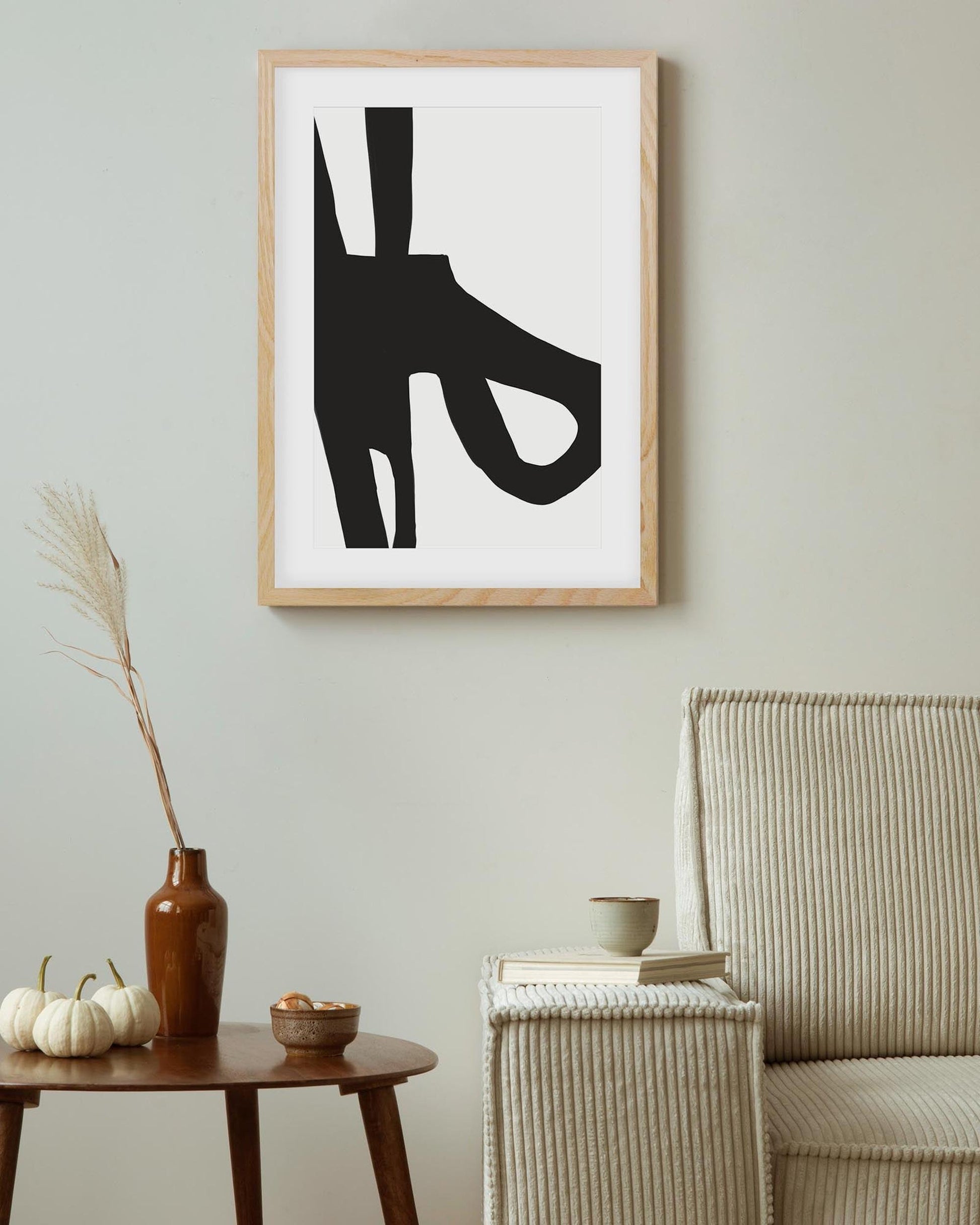 Framed abstract black and white artwork on a wall above a wooden side table with decorative items.