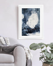 Framed abstract art print on a wall above a sofa with a plant in the corner.