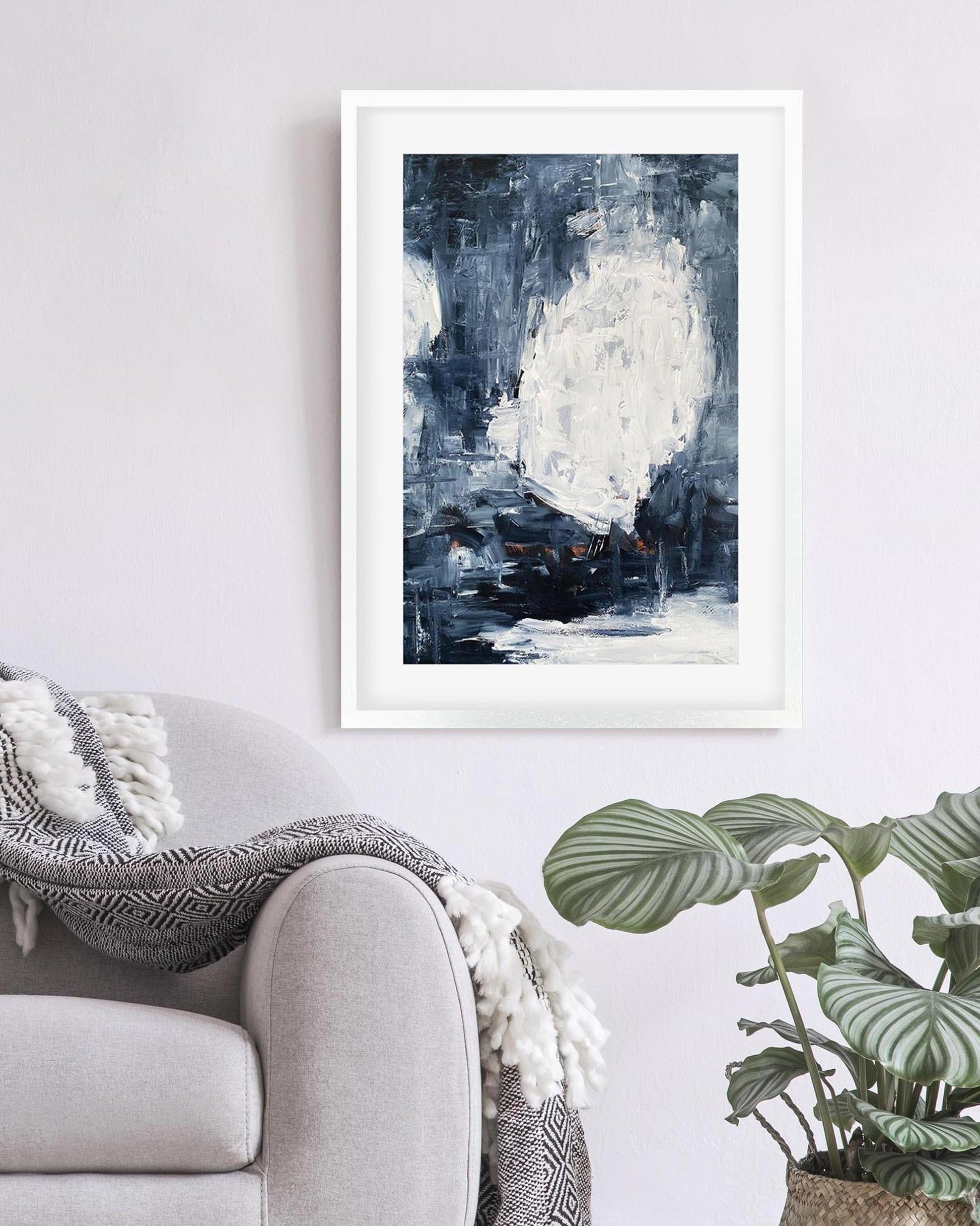 Framed abstract art print on a wall above a sofa with a plant in the corner.