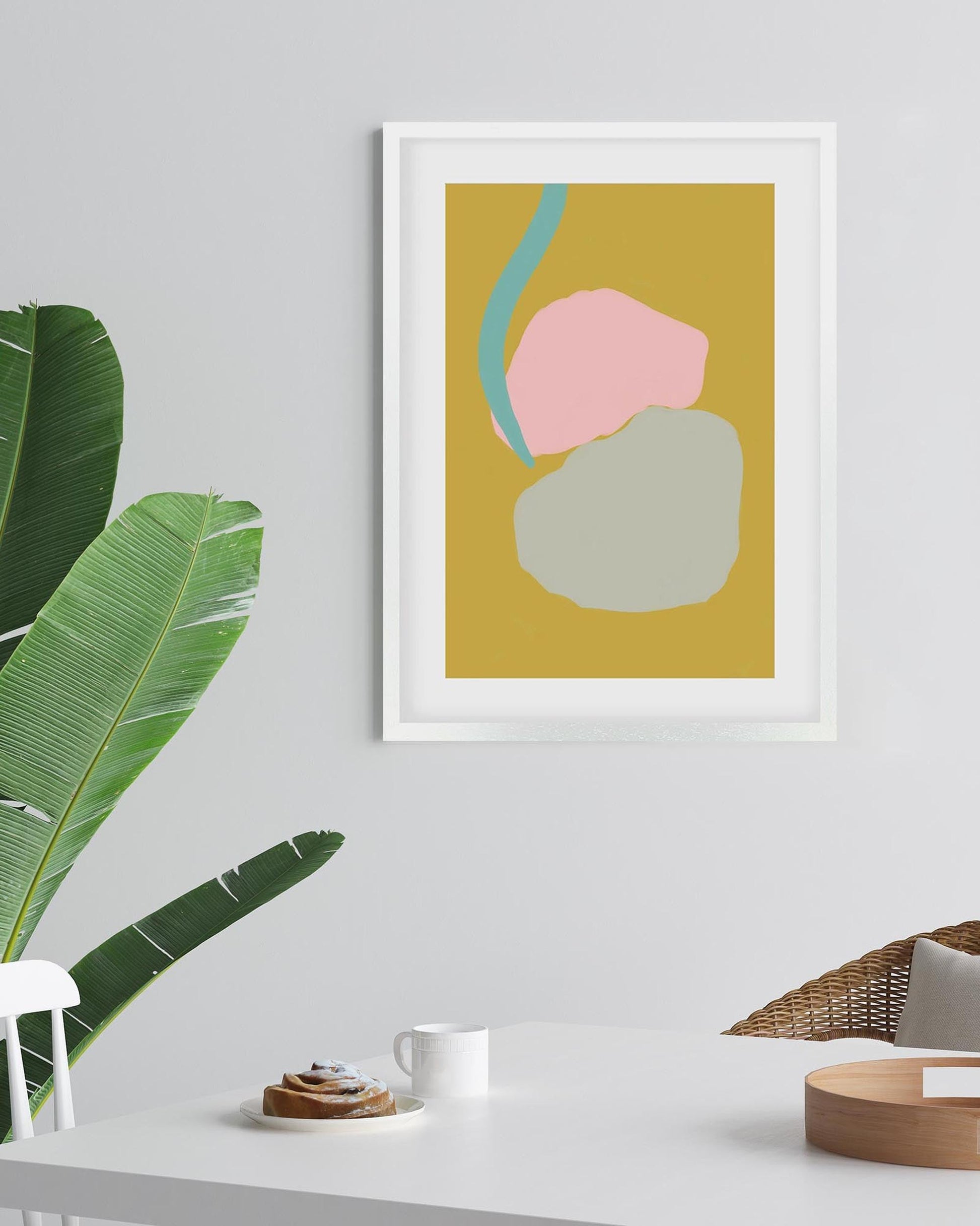 Framed abstract art print on a wall with a plant and table in the foreground