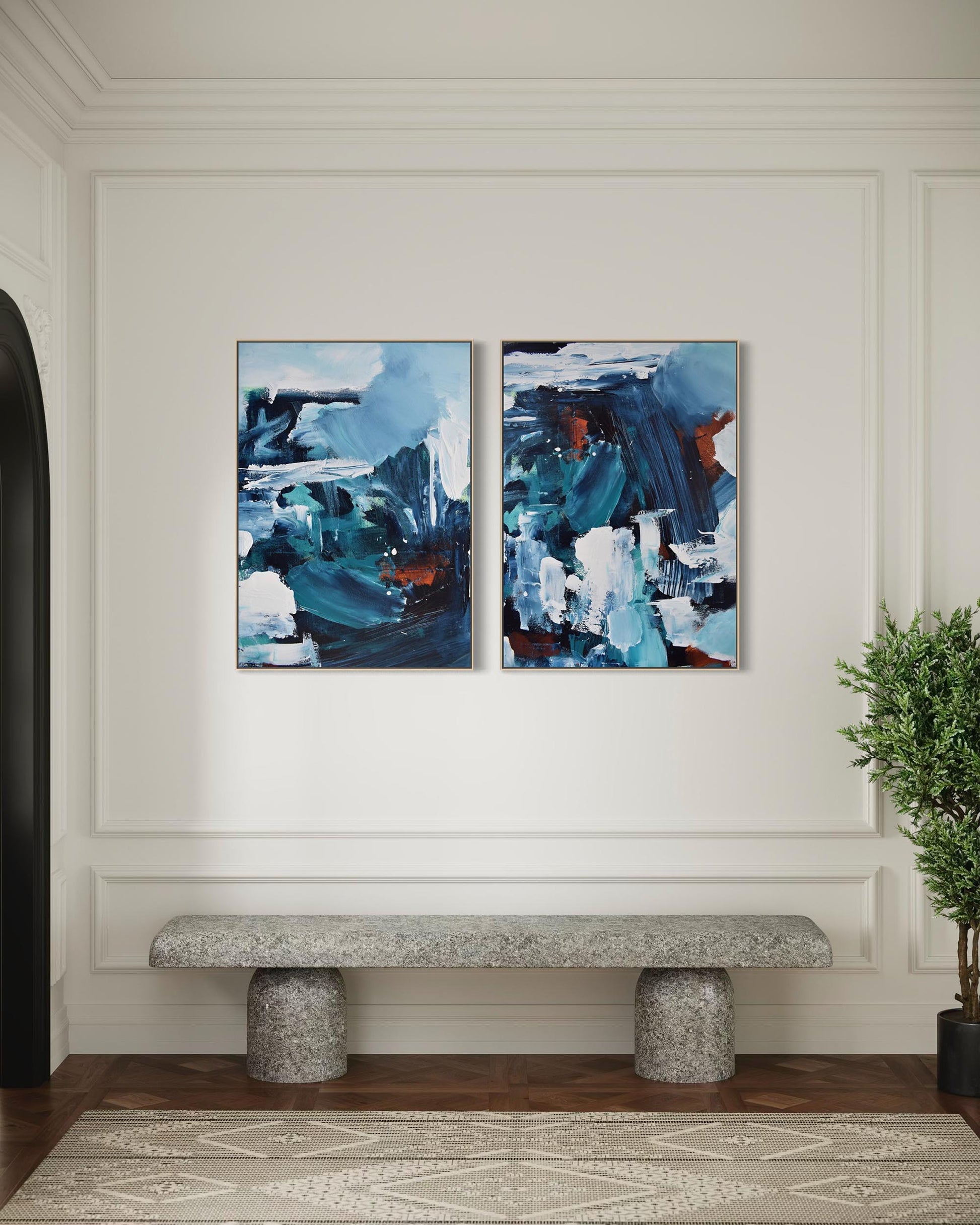Two abstract blue artworks on a wall above a stone bench with a plant to the side.