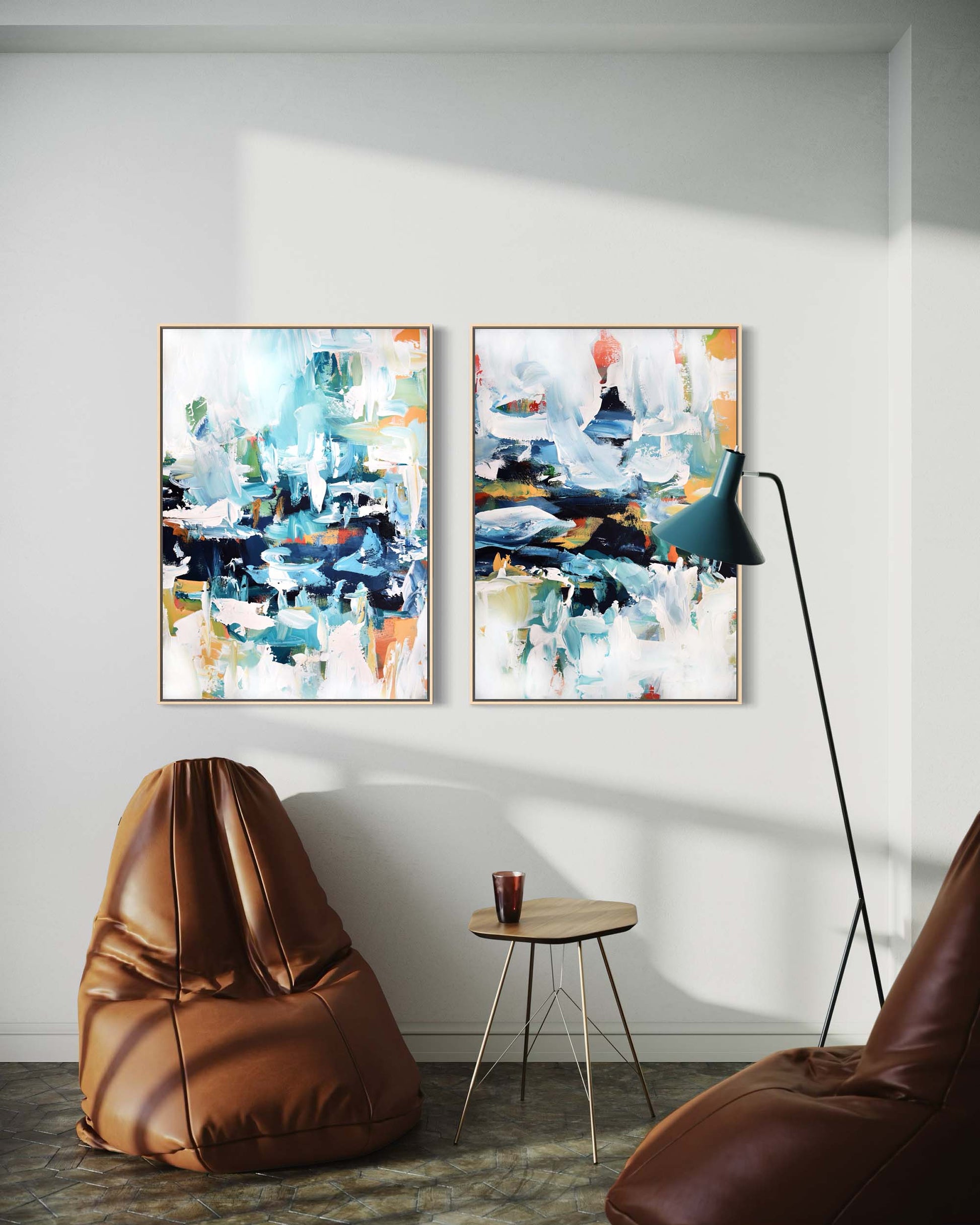 Two abstract paintings on a wall above a brown bean bag chair and small table.