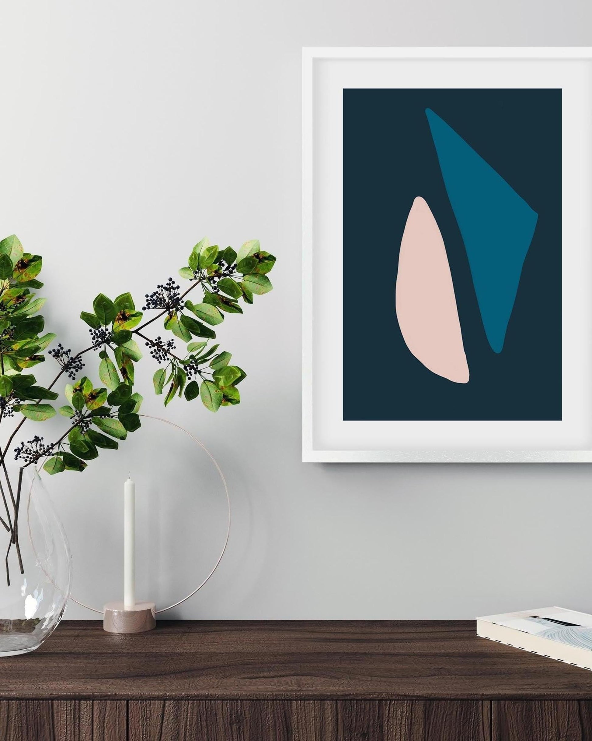 Framed abstract art print on a wall above a wooden surface with a plant and candle.