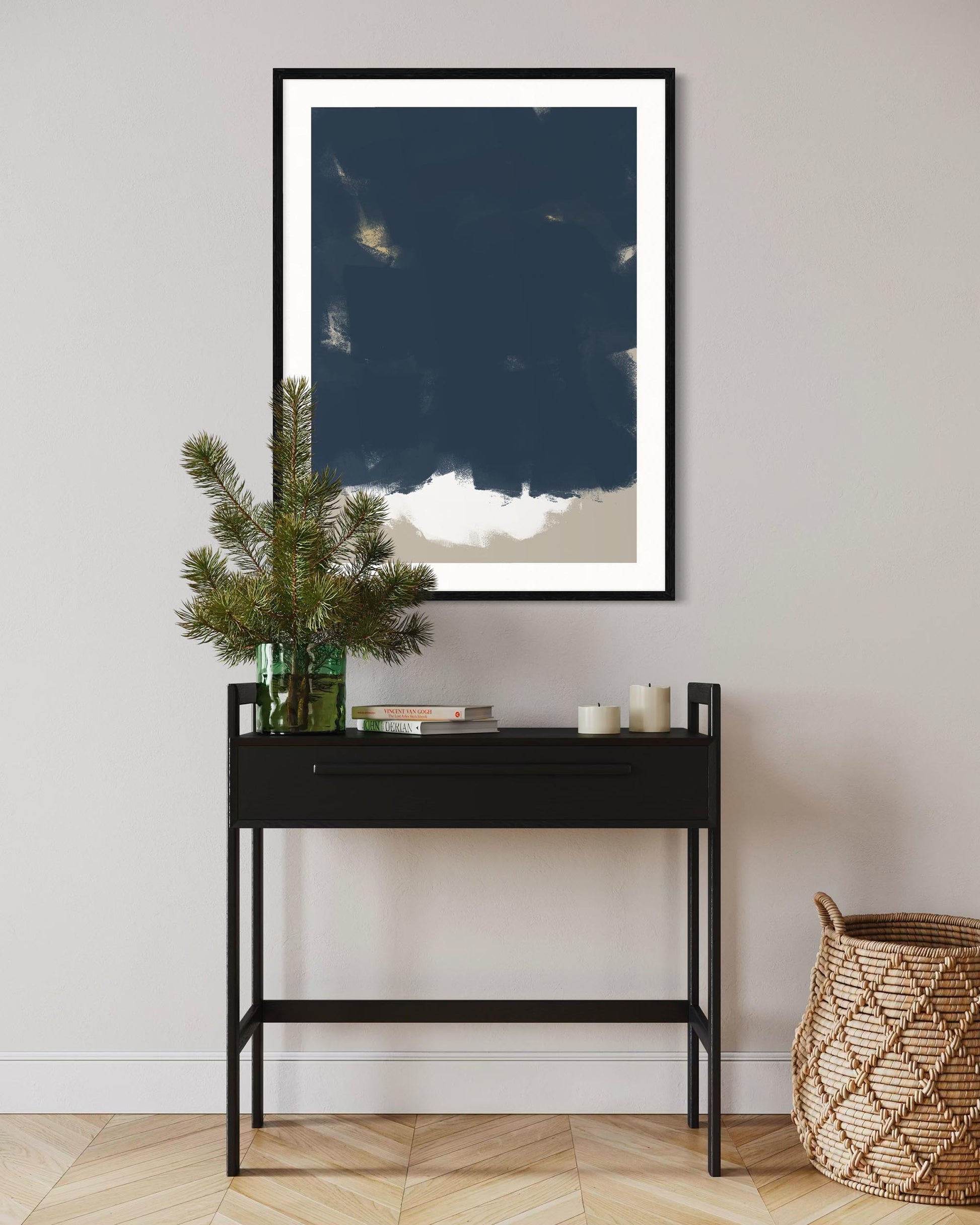 Framed artwork of a blue sky with clouds on a wall above a black console table with decorative items.