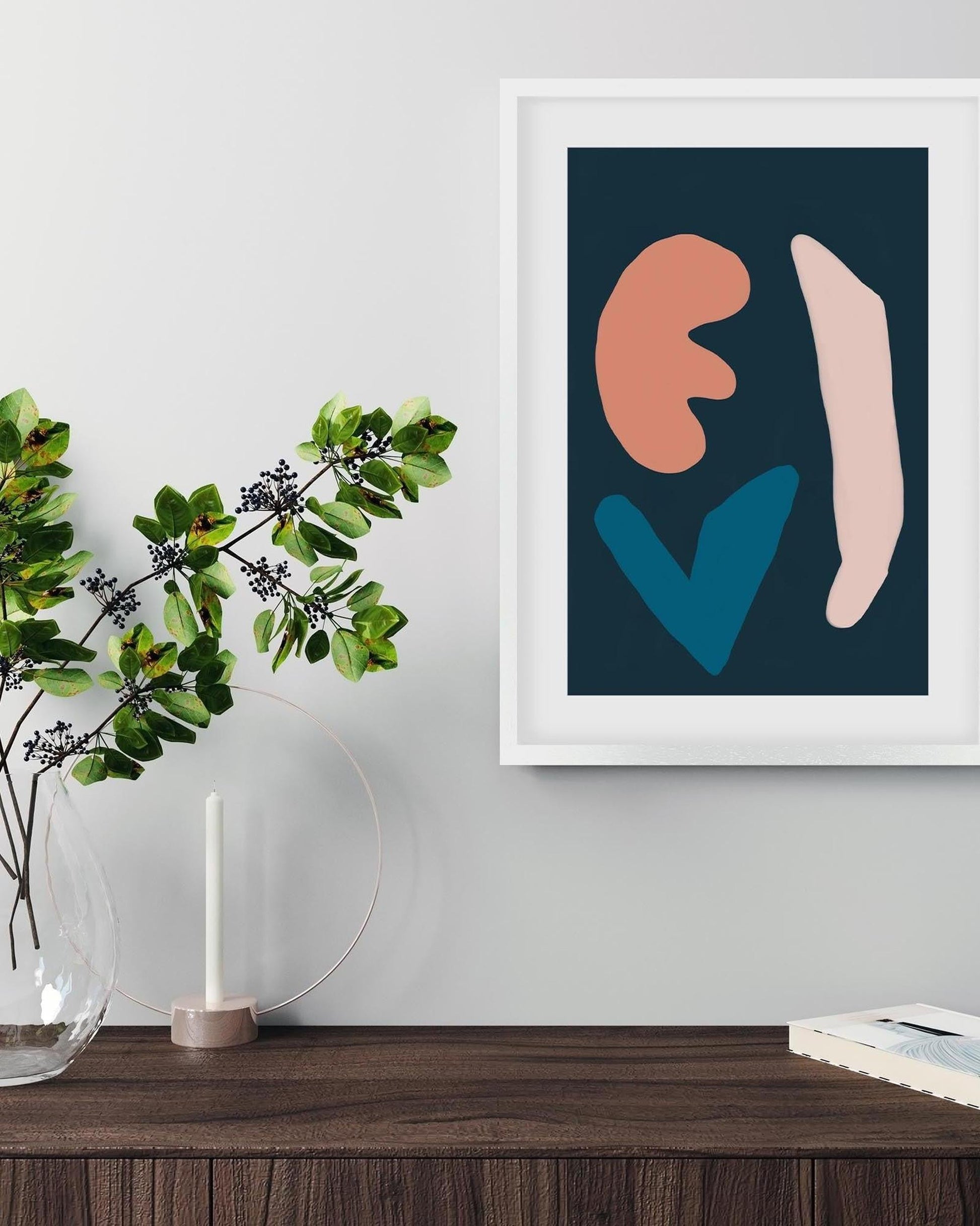 Framed abstract art print on a wall above a wooden surface with a plant and candle.
