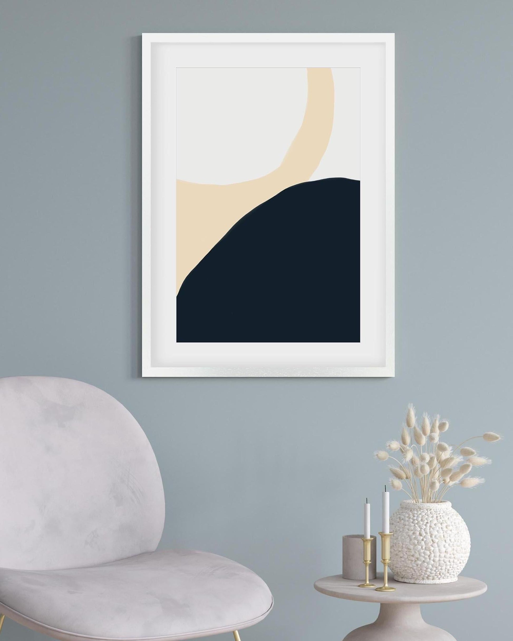 Framed abstract art piece on a wall with a chair and decorative items below.