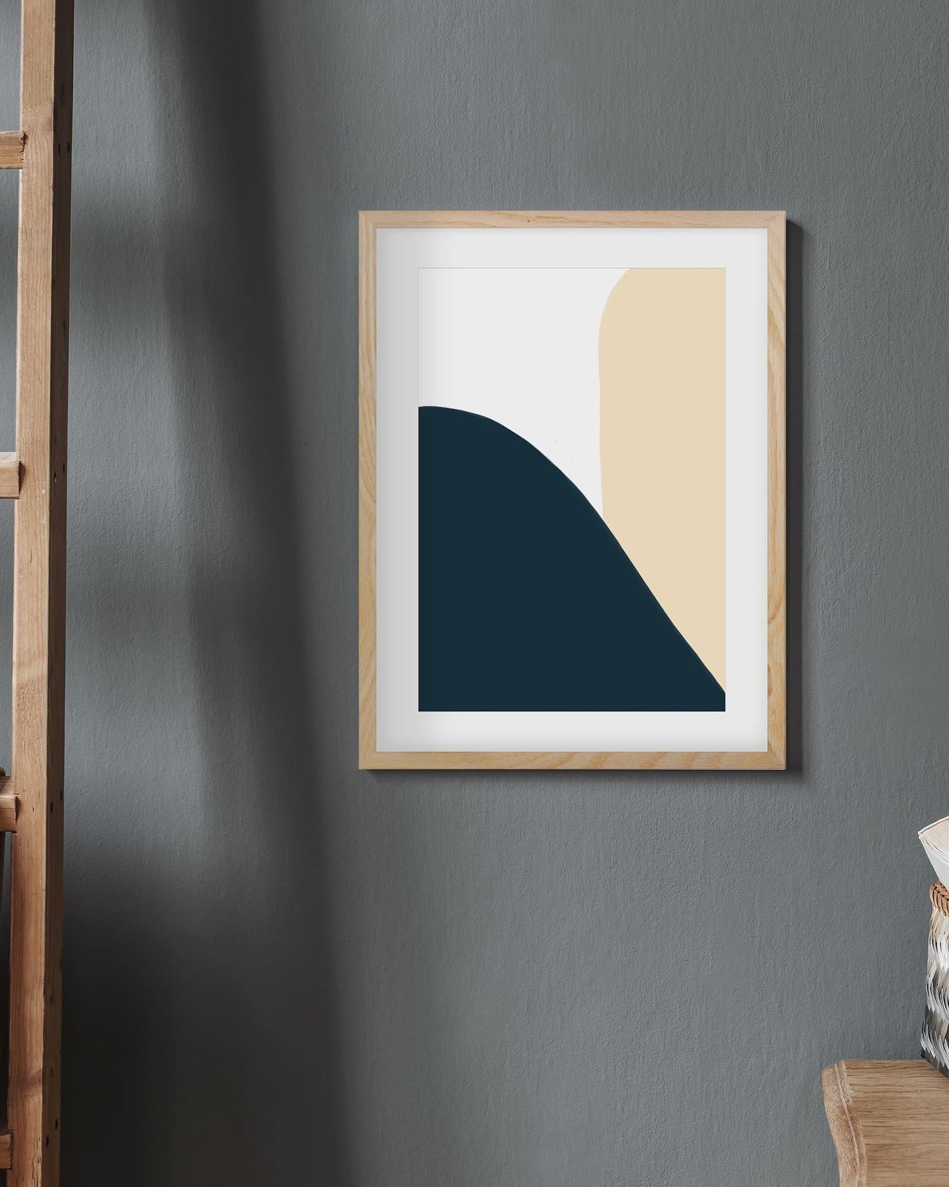 Framed abstract art piece on a gray wall with a wooden ladder and chair in the corner.