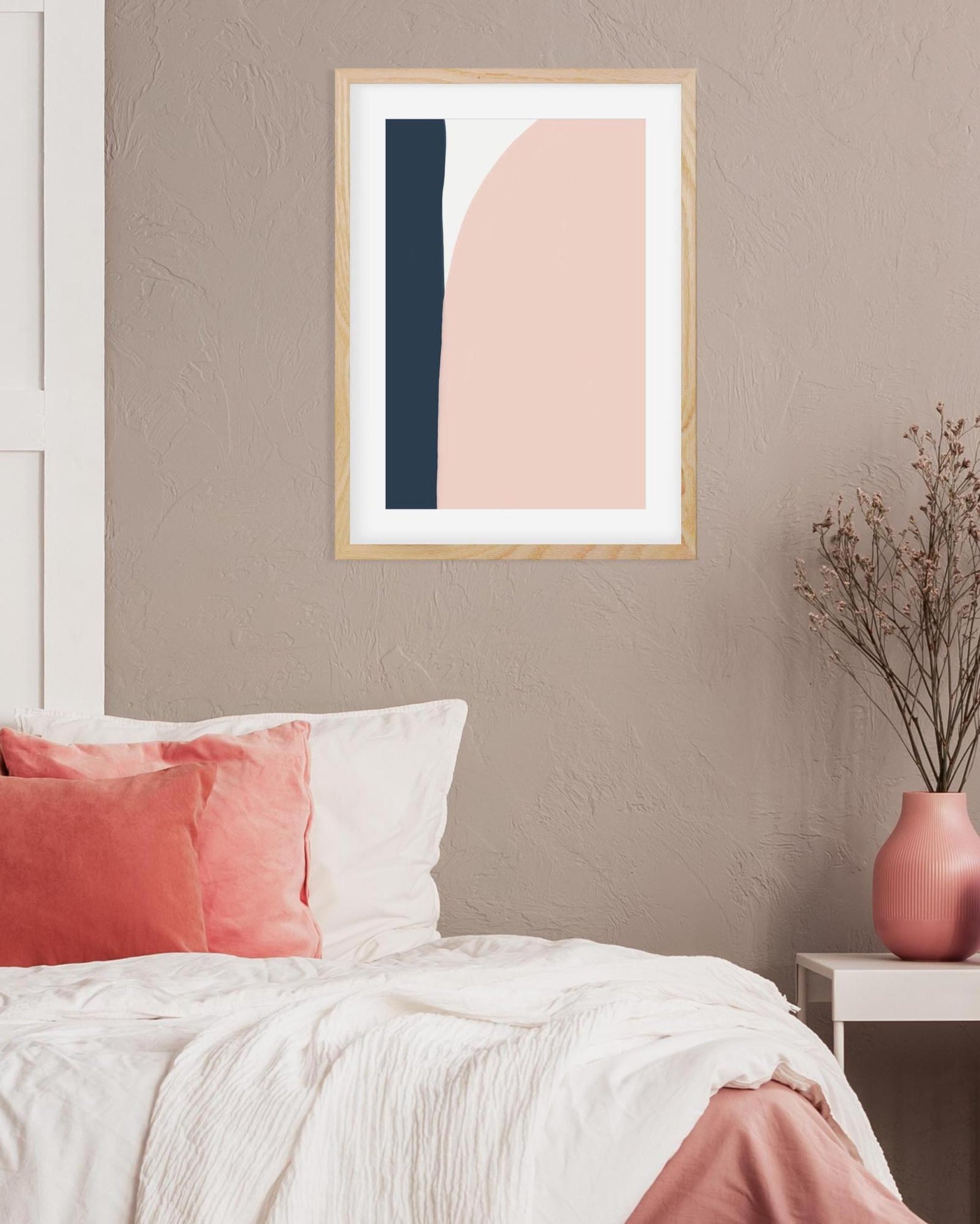 Abstract art print in a wooden frame on a wall above a bed with pink and white bedding.
