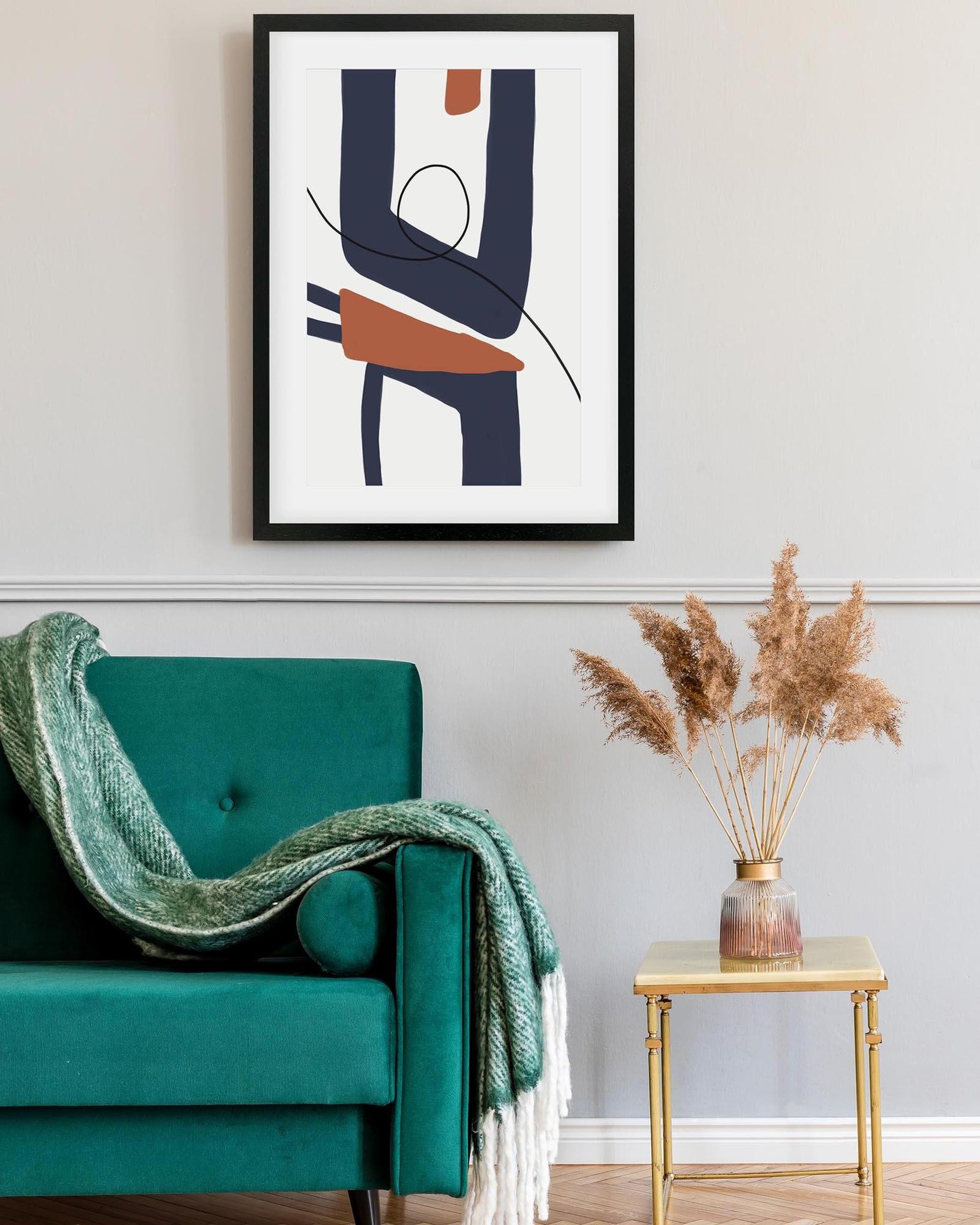 Teal armchair with a green blanket, abstract art on the wall, and a small table with dried plants.