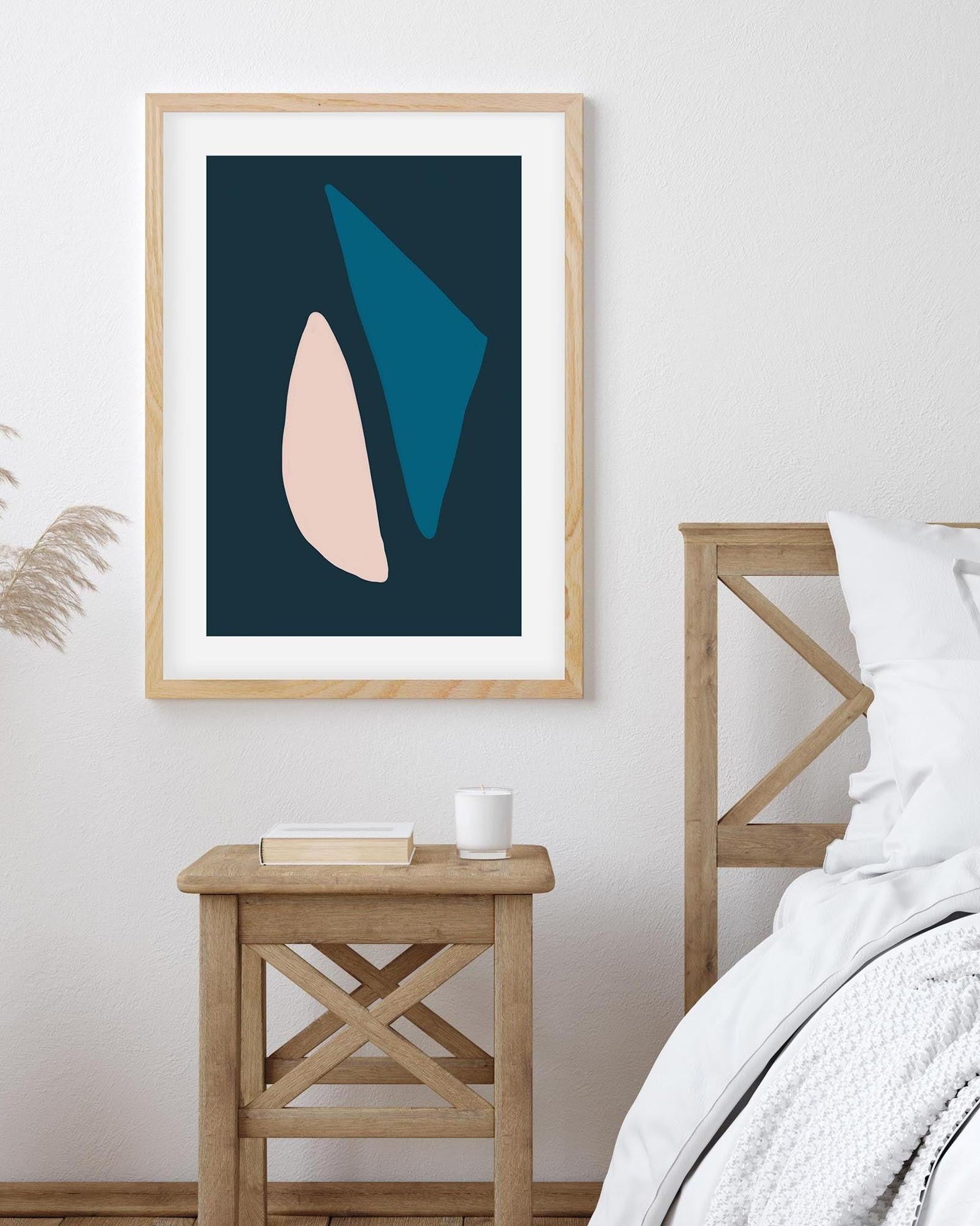Framed abstract art print on a wall above a wooden side table in a bedroom.