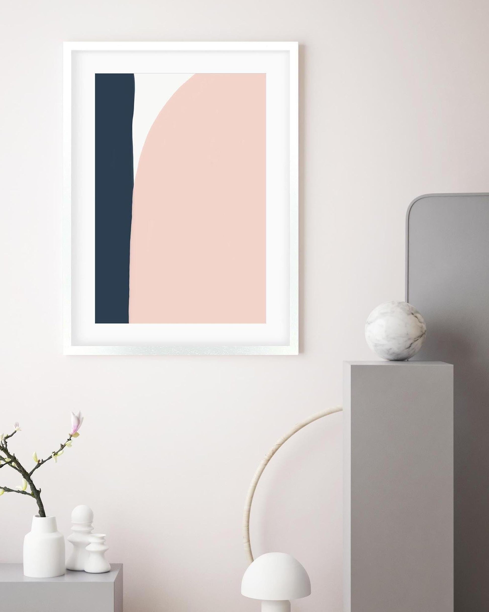 Framed abstract art print with pink and blue shapes on a wall in a minimalistic room.