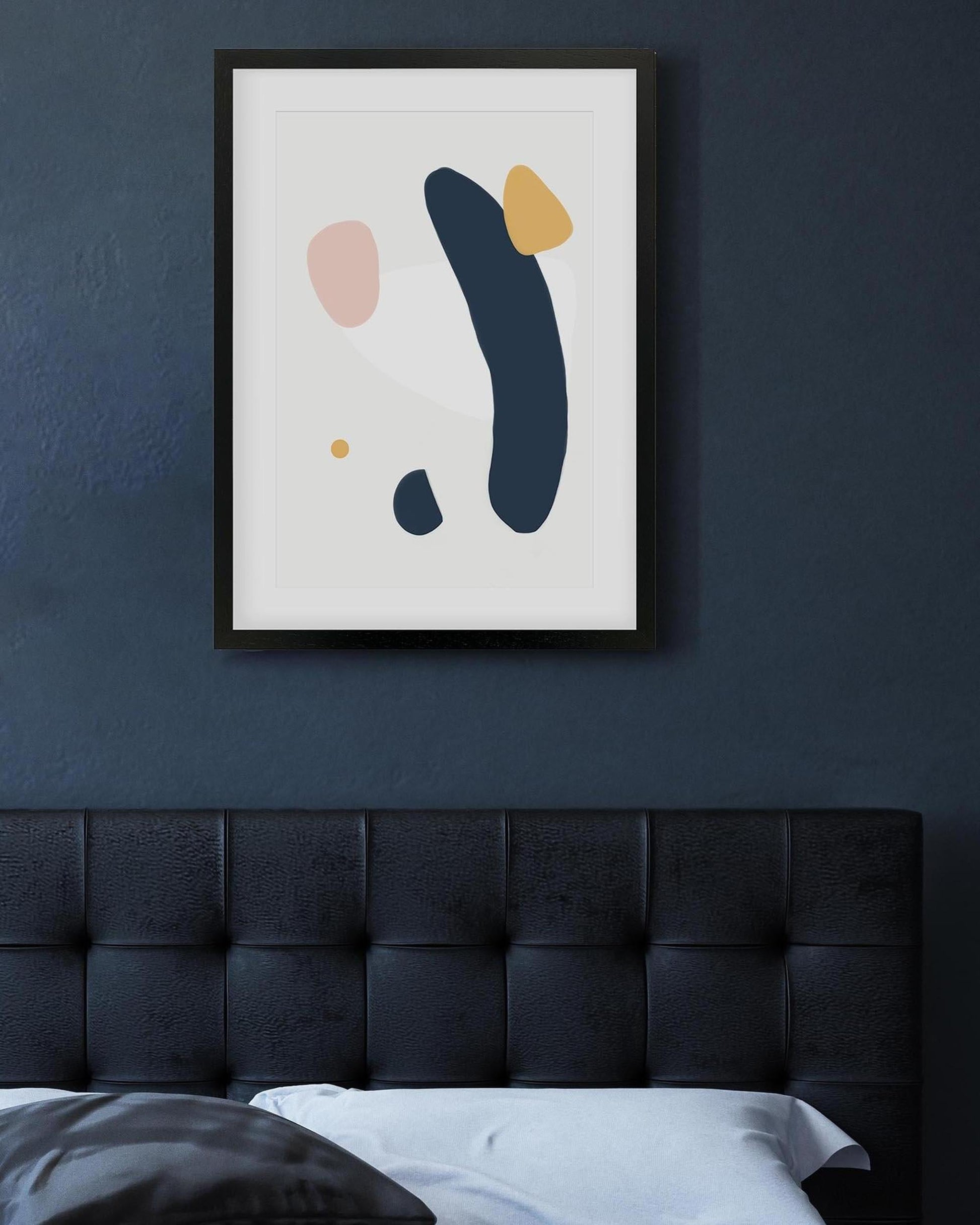 Abstract art print on a dark blue wall above a bed with a tufted headboard.