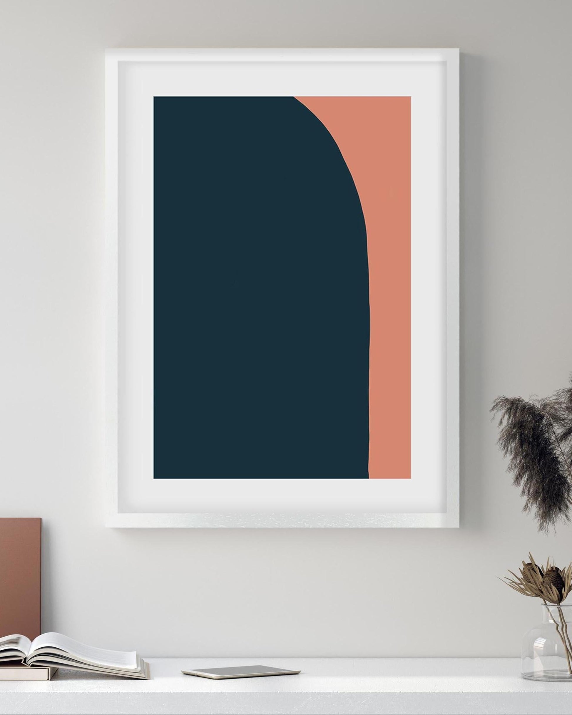 Framed abstract art print with blue and orange shapes on a white wall.
