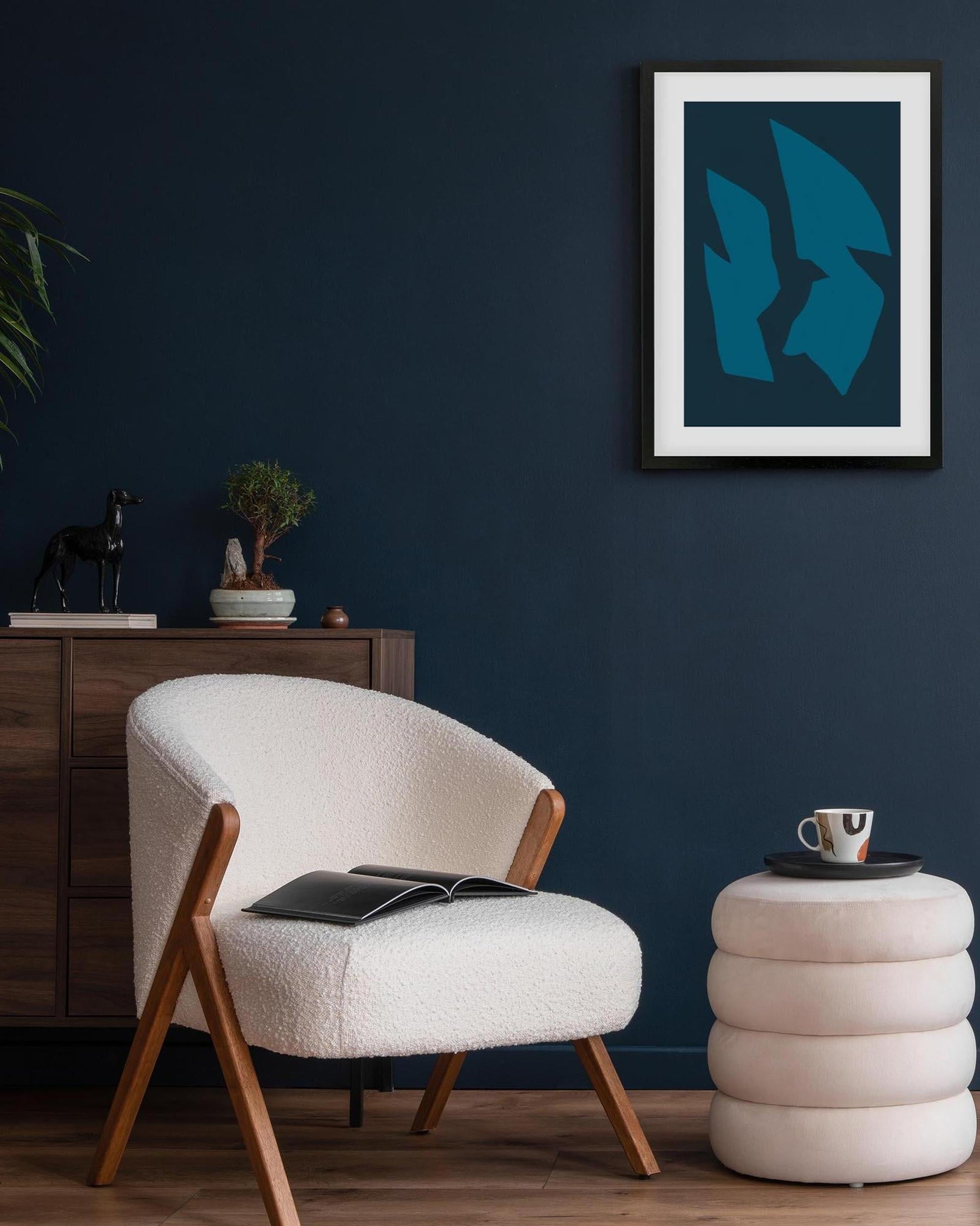 Modern living room with a white armchair, side table, and abstract blue artwork on a dark blue wall.