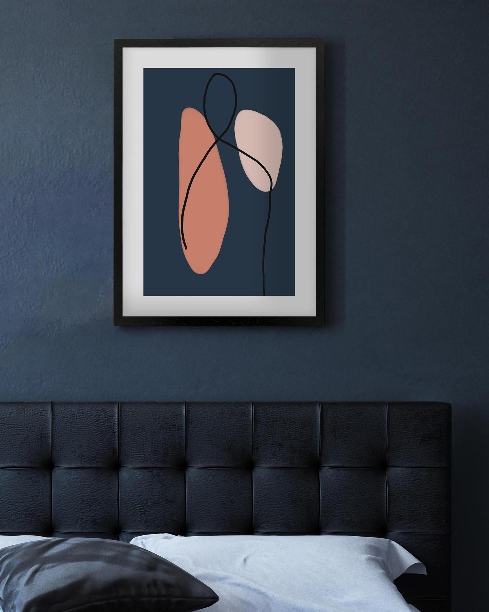 Abstract art print on a dark blue wall above a bed with a tufted headboard.