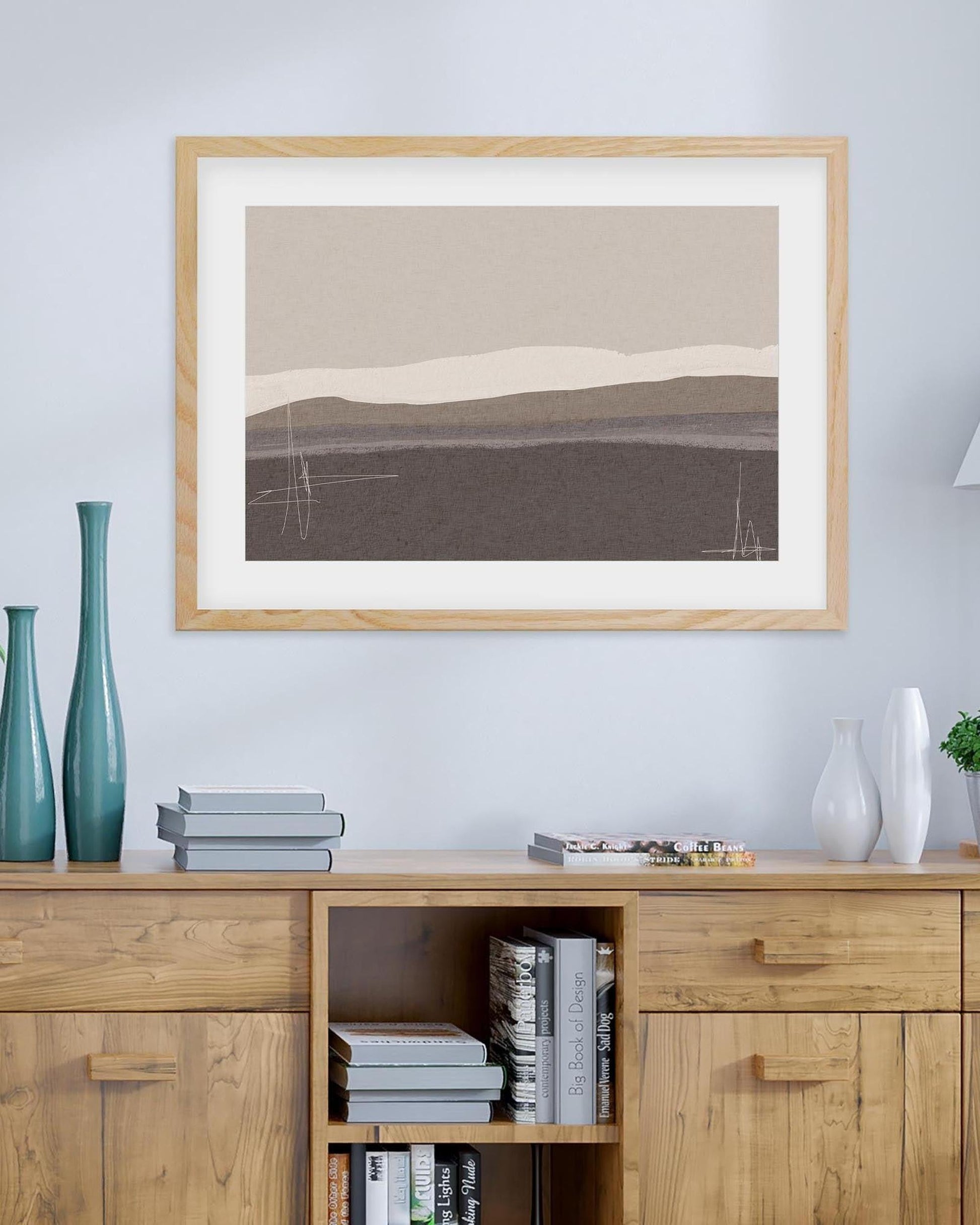 Framed abstract art piece on a wall above a wooden cabinet with books and decor items.