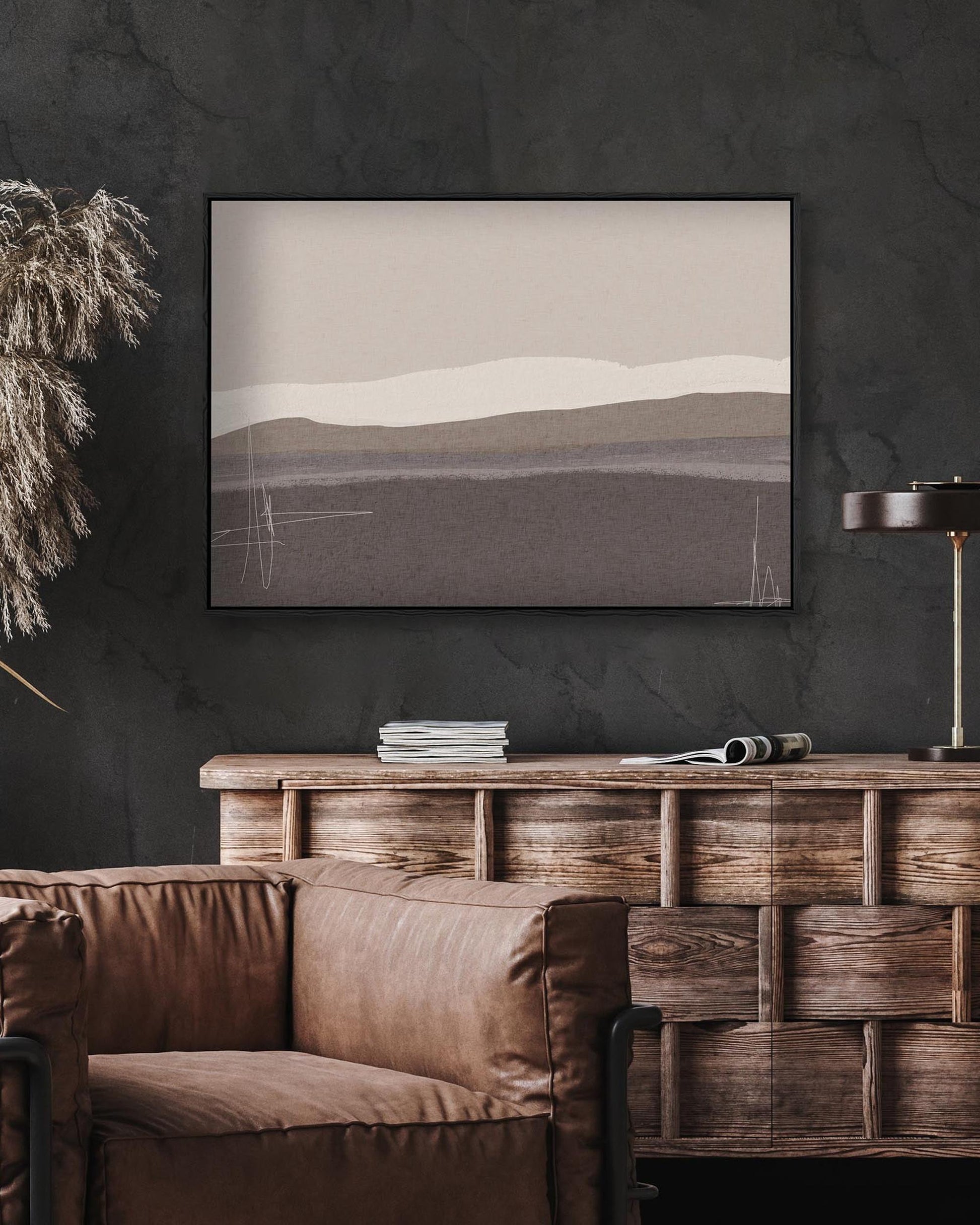 Framed landscape painting on a dark wall above a wooden console table with a brown sofa.