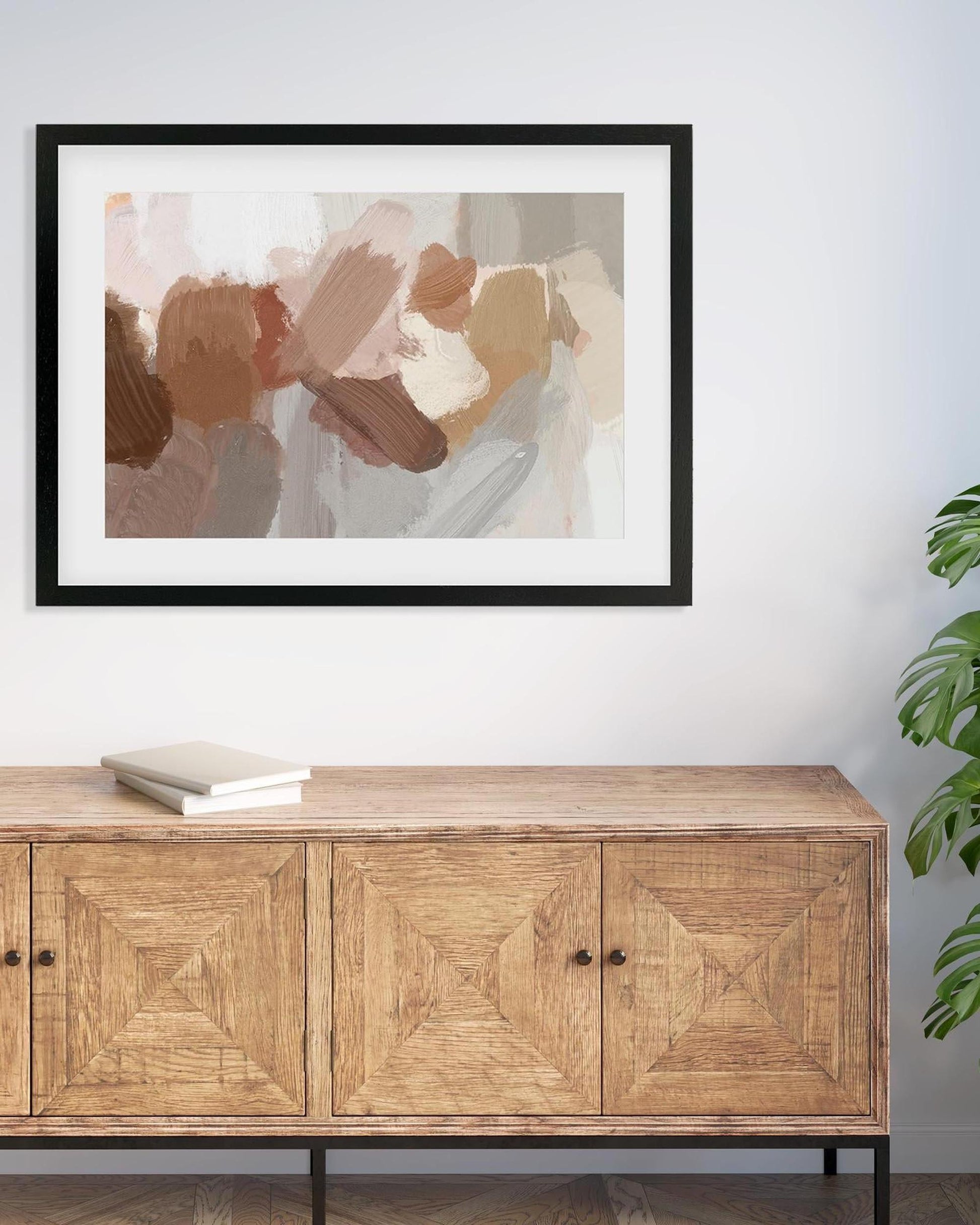 Framed abstract art above a wooden sideboard with a plant to the right.