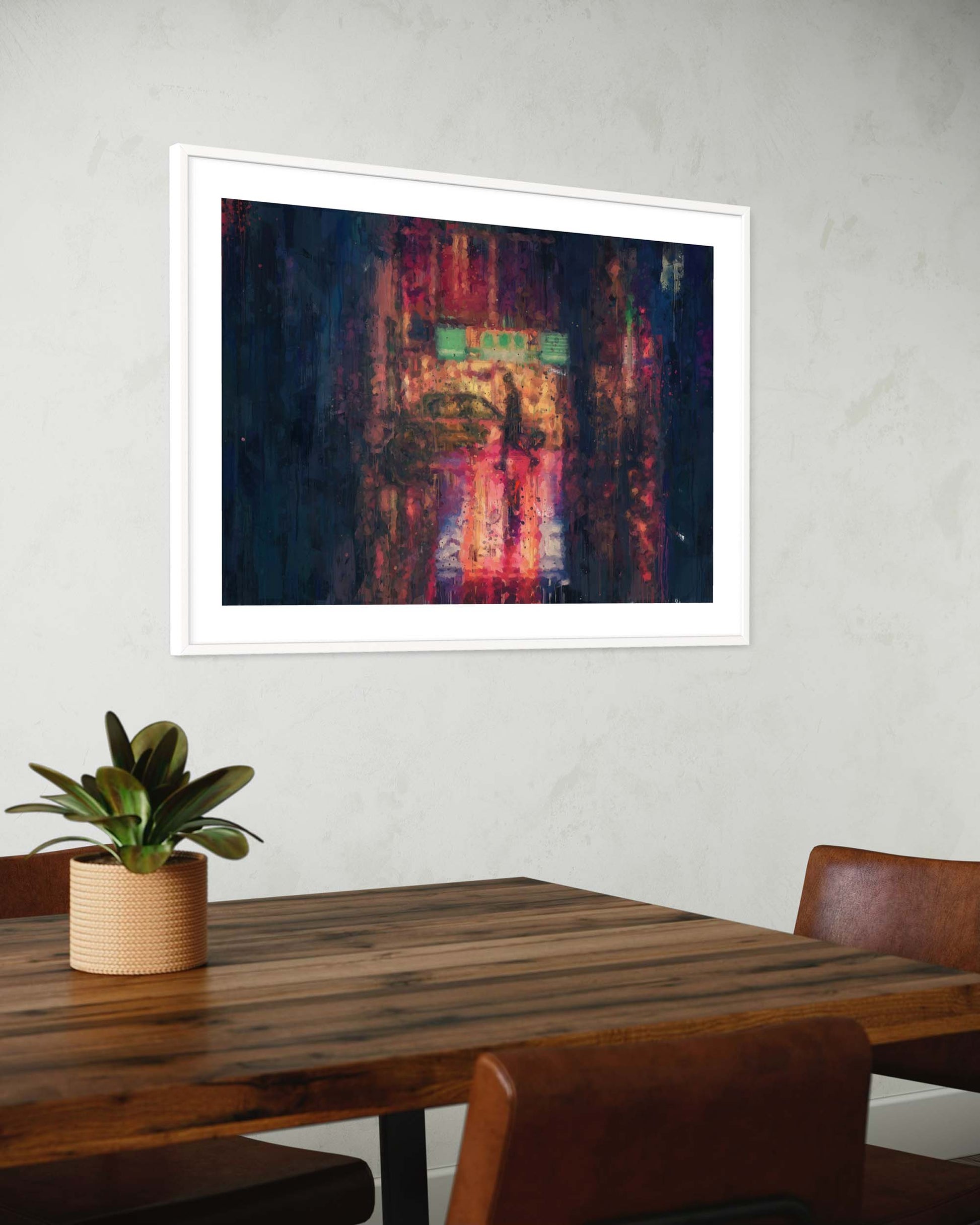Abstract painting in a white frame on a wall above a wooden table with a plant.