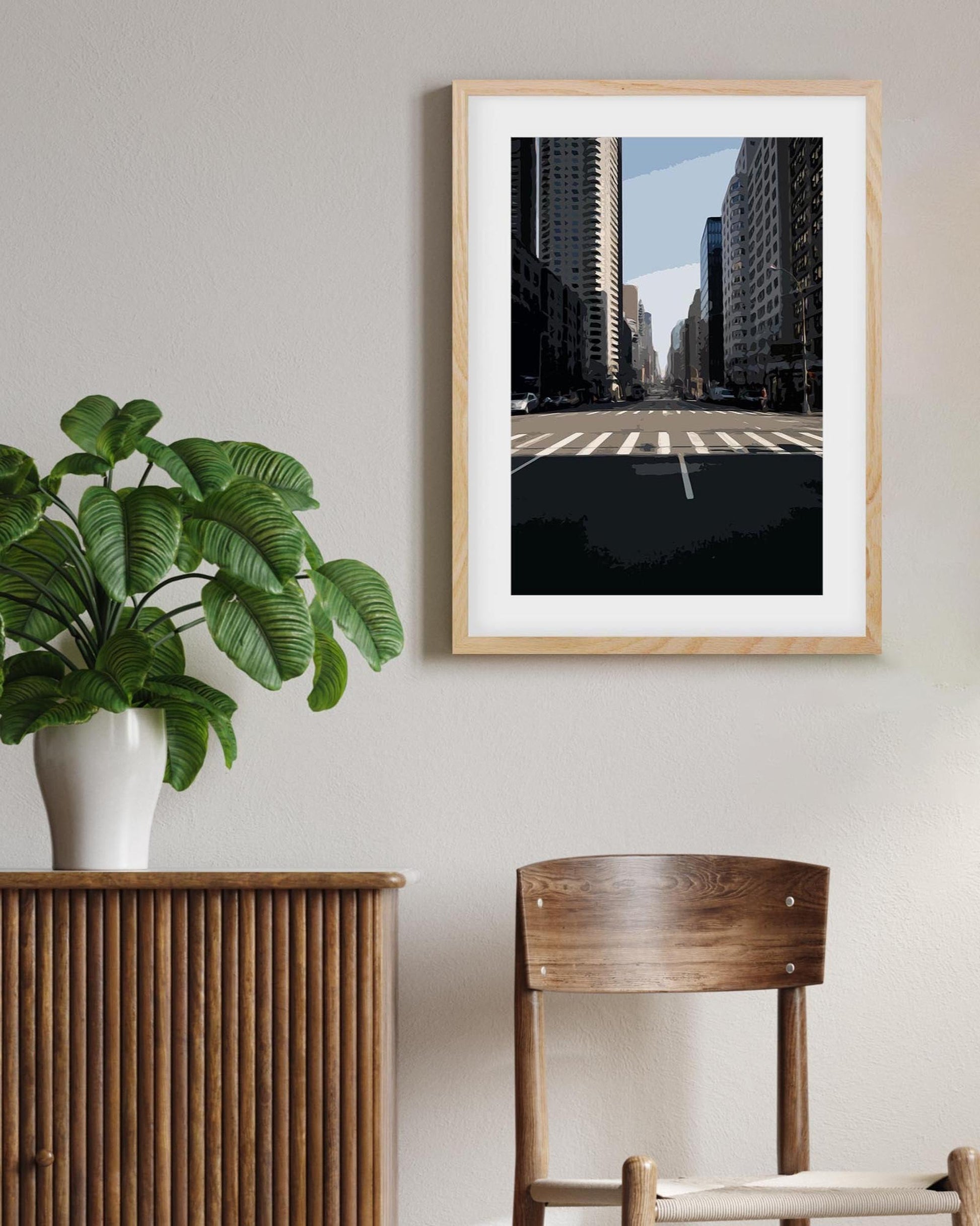 Framed cityscape print on a wall with a plant and wooden furniture.