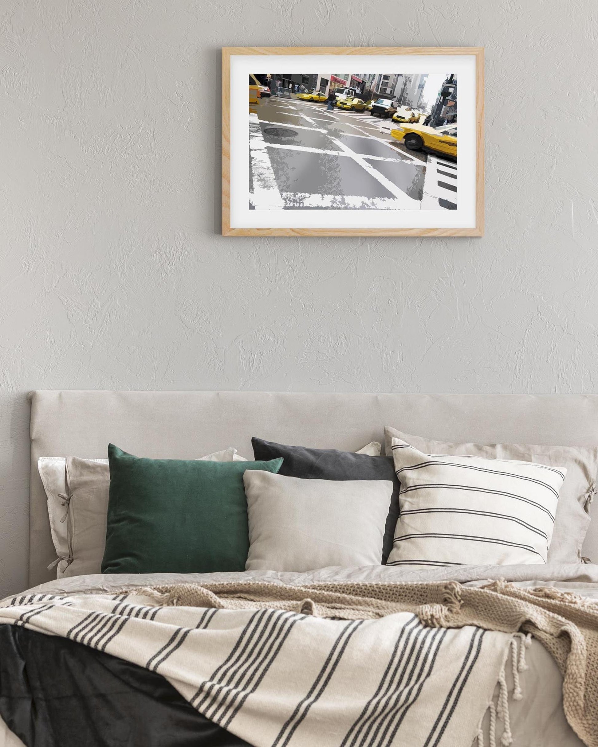 Framed artwork of a city street scene with taxis above a bed with decorative pillows and blankets.