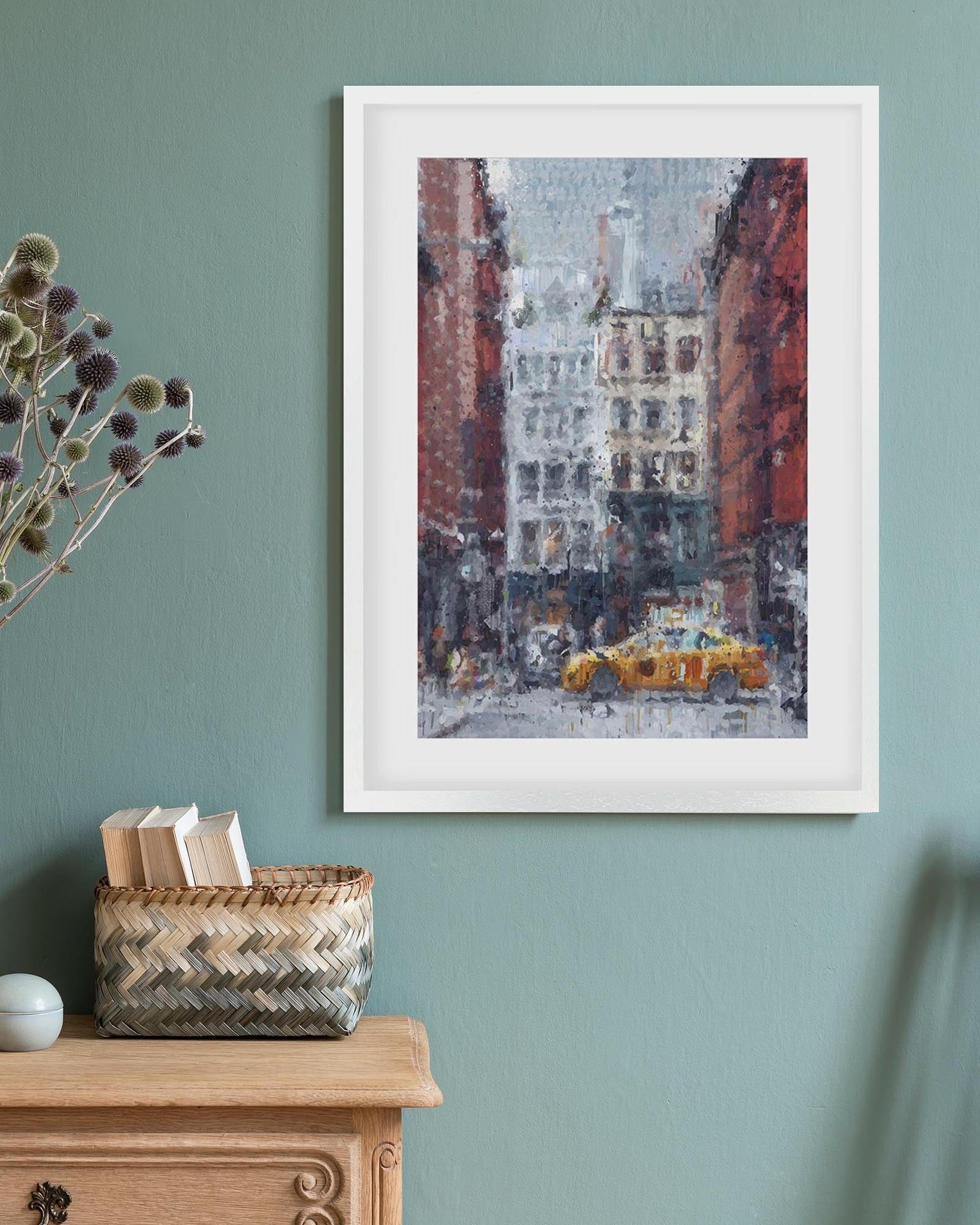 Framed artwork of a snowy city street with a yellow taxi on a teal wall above a wooden cabinet.