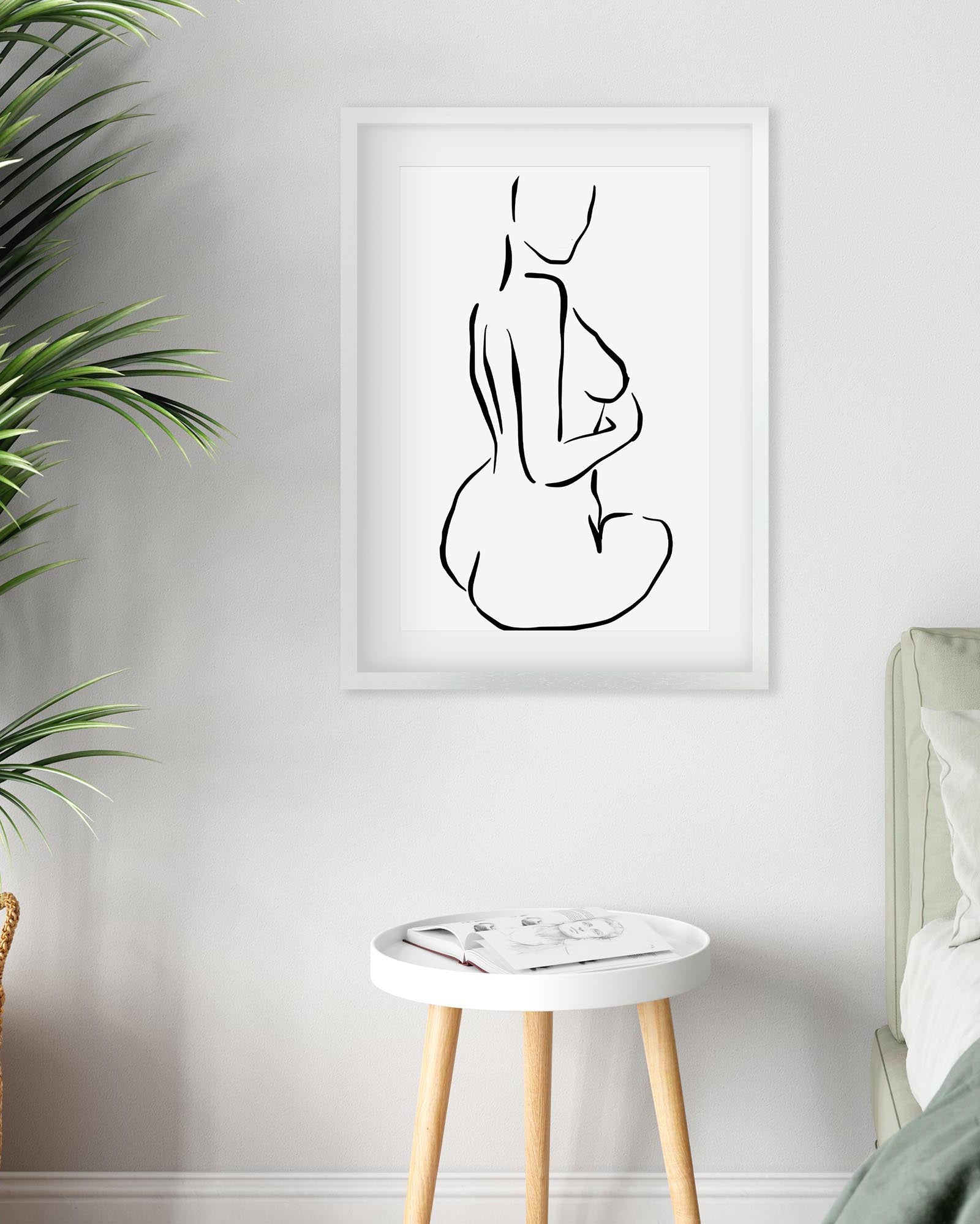 Minimalist line art of a nude figure on a white wall above a small table.