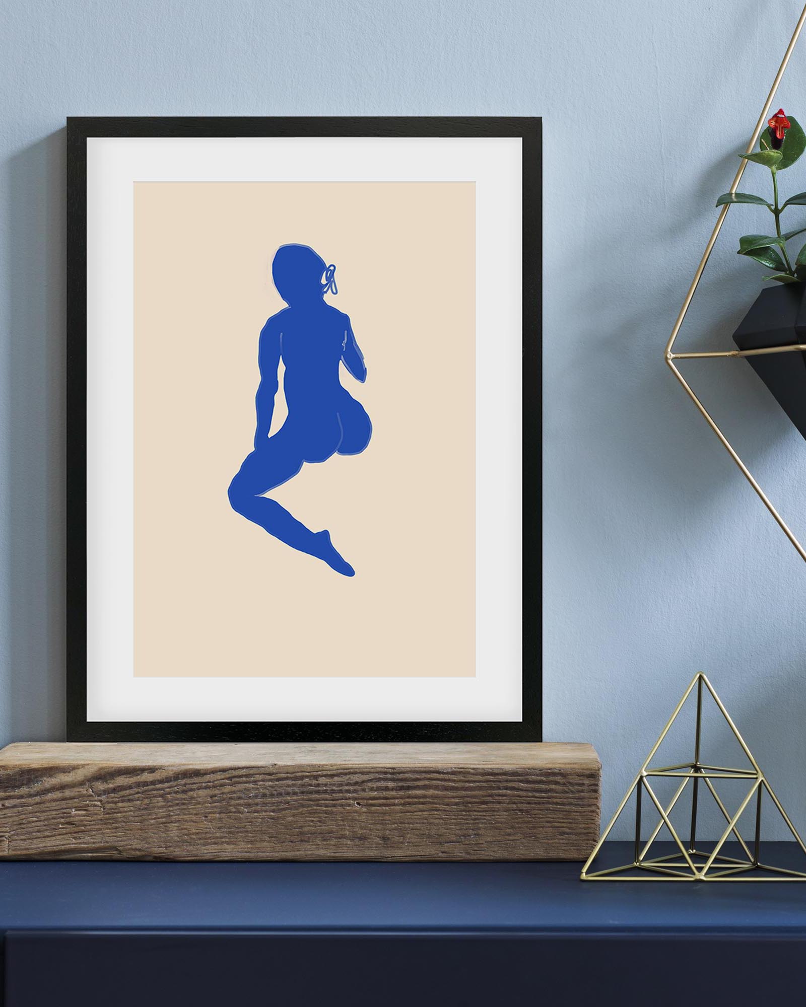 Framed artwork with a blue silhouette of a person on a beige background, displayed on a shelf against a light blue wall.