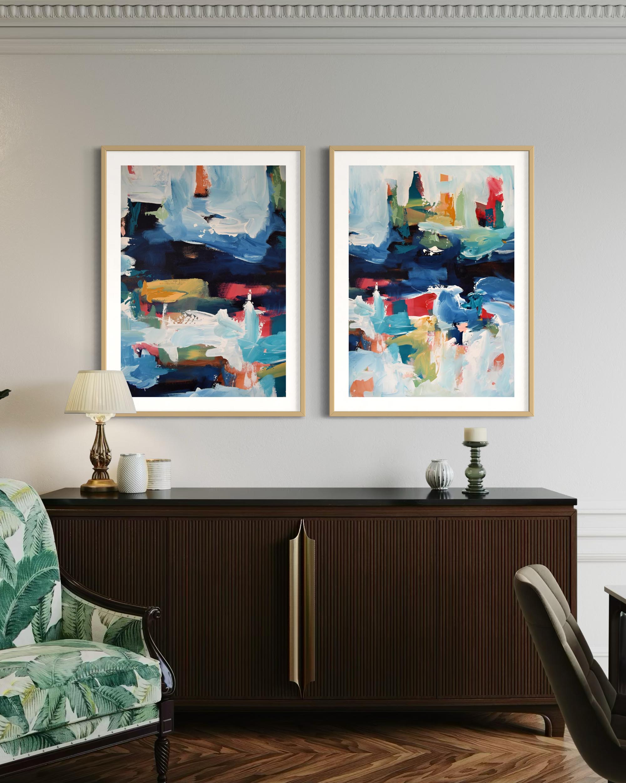 Two abstract paintings in gold frames on a wall above a dark wooden cabinet.