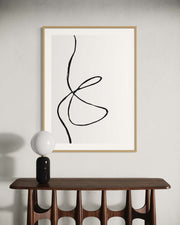 Abstract line art in a wooden frame on a white wall above a wooden console table.