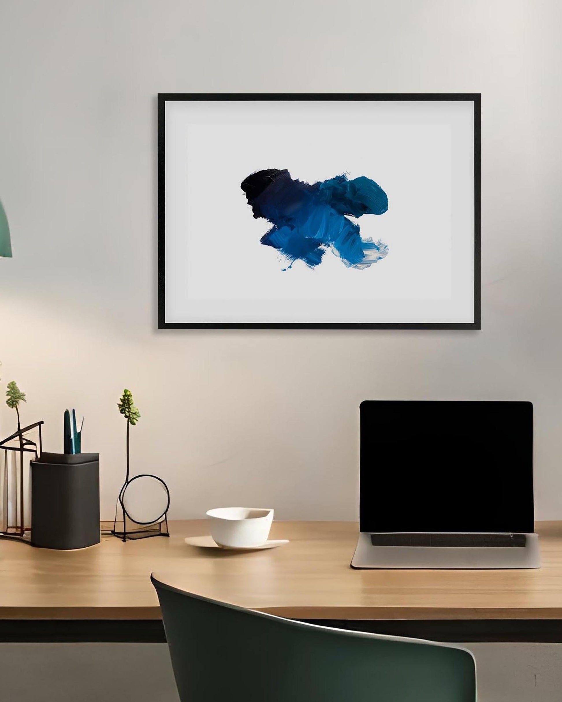Framed abstract art piece on a wall above a desk with a laptop and decor items.