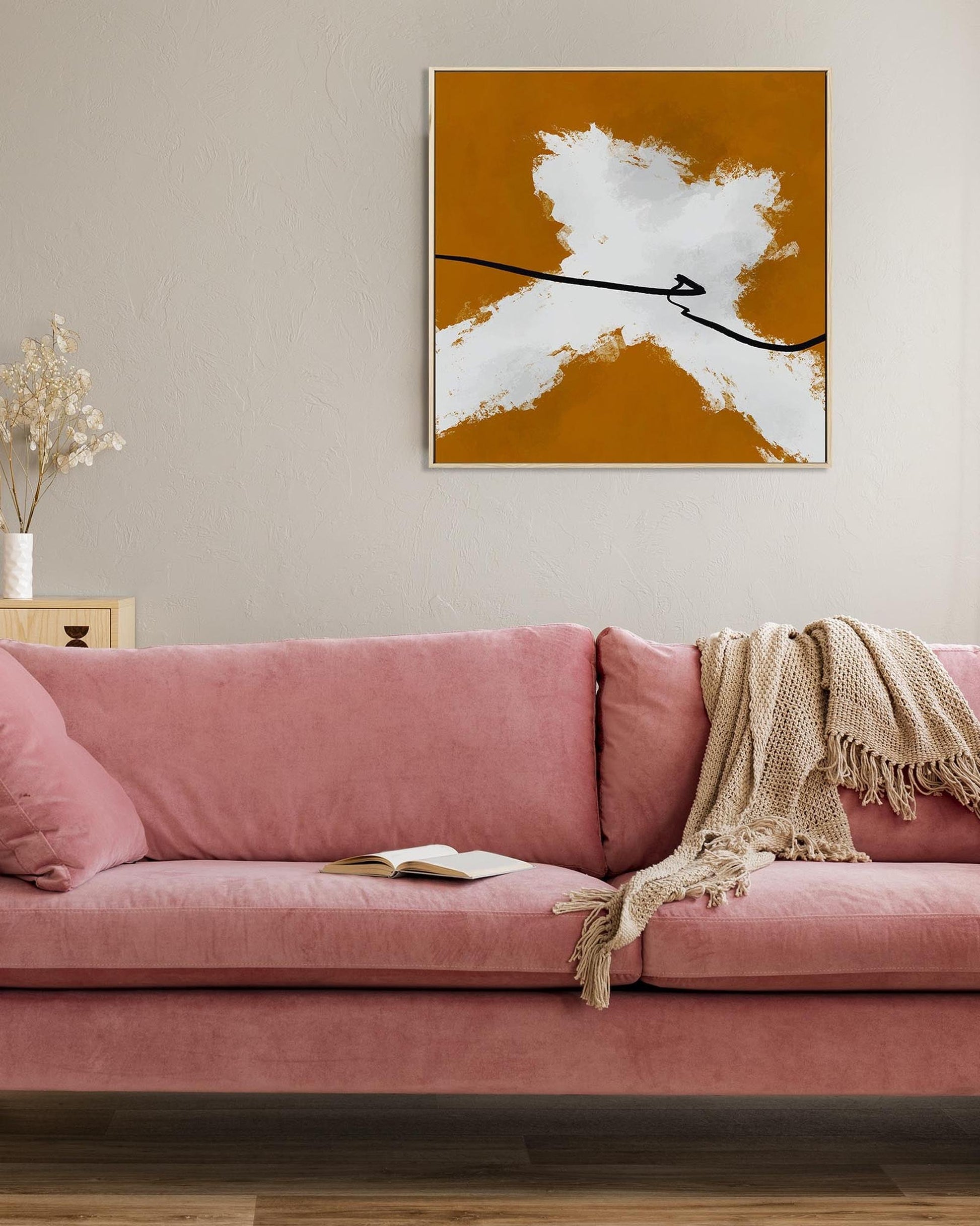 Pink sofa with a blanket and book in a room with a abstract painting on the wall.