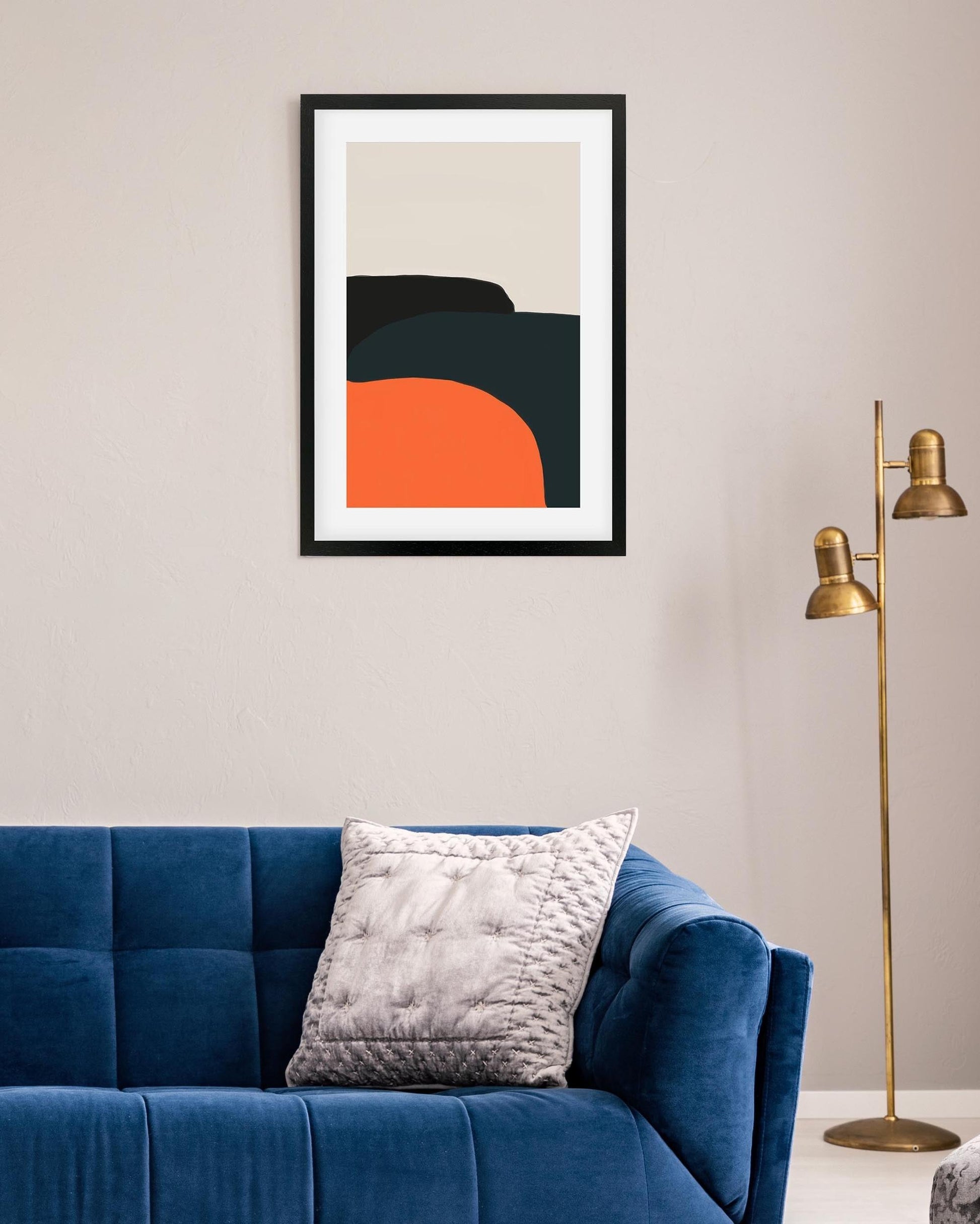 Framed abstract art piece on a wall above a blue sofa with a gold floor lamp.