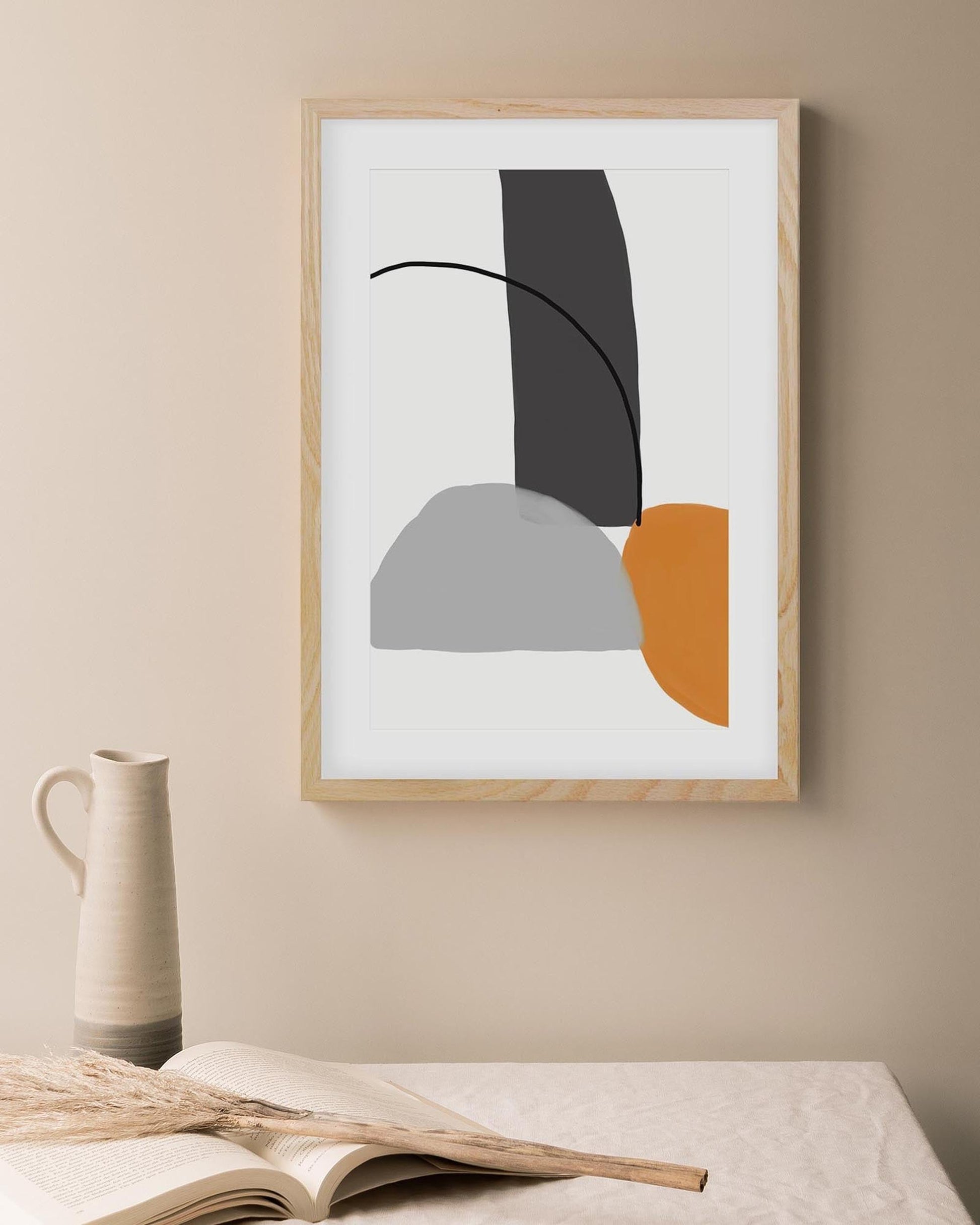 Framed abstract art piece on a wall with a vase and book in the foreground.