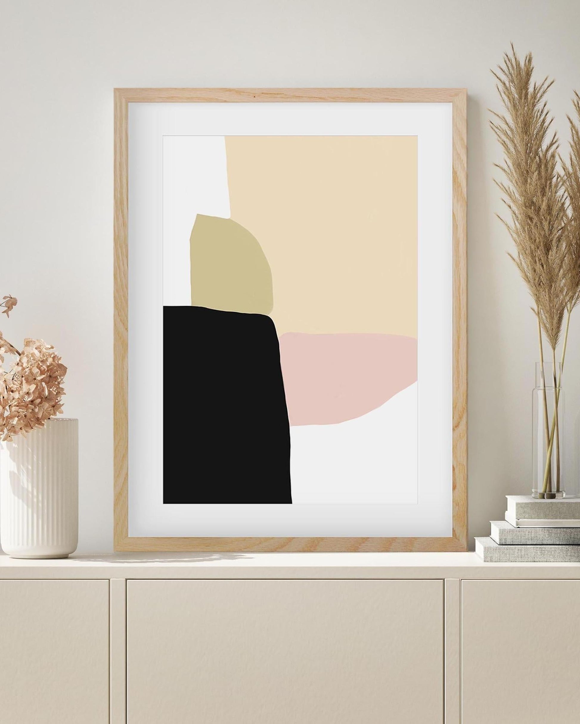 Framed abstract art print with geometric shapes on a wall above a cabinet.