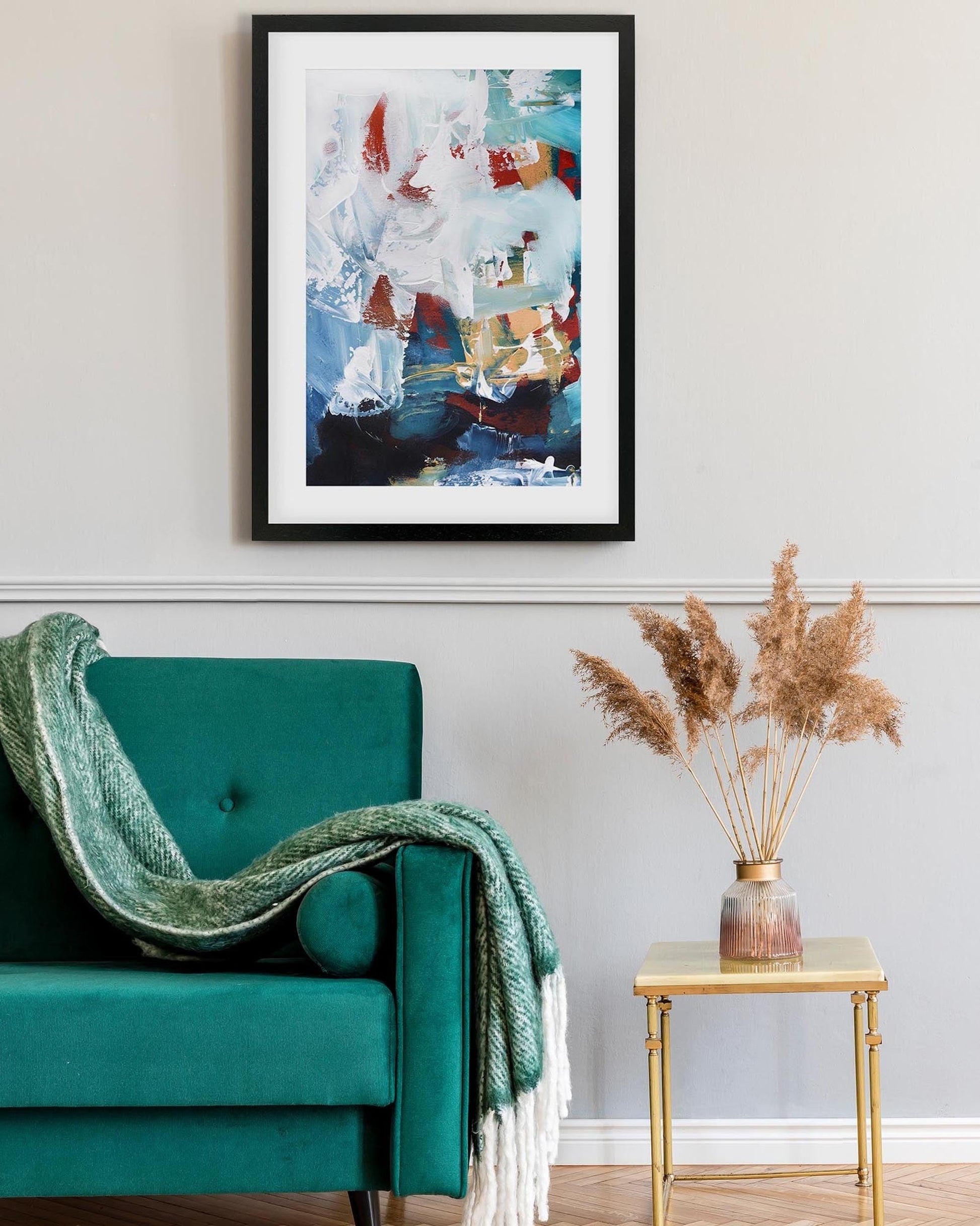 Teal armchair with a green blanket, abstract painting on the wall, and a small table with dried plants.