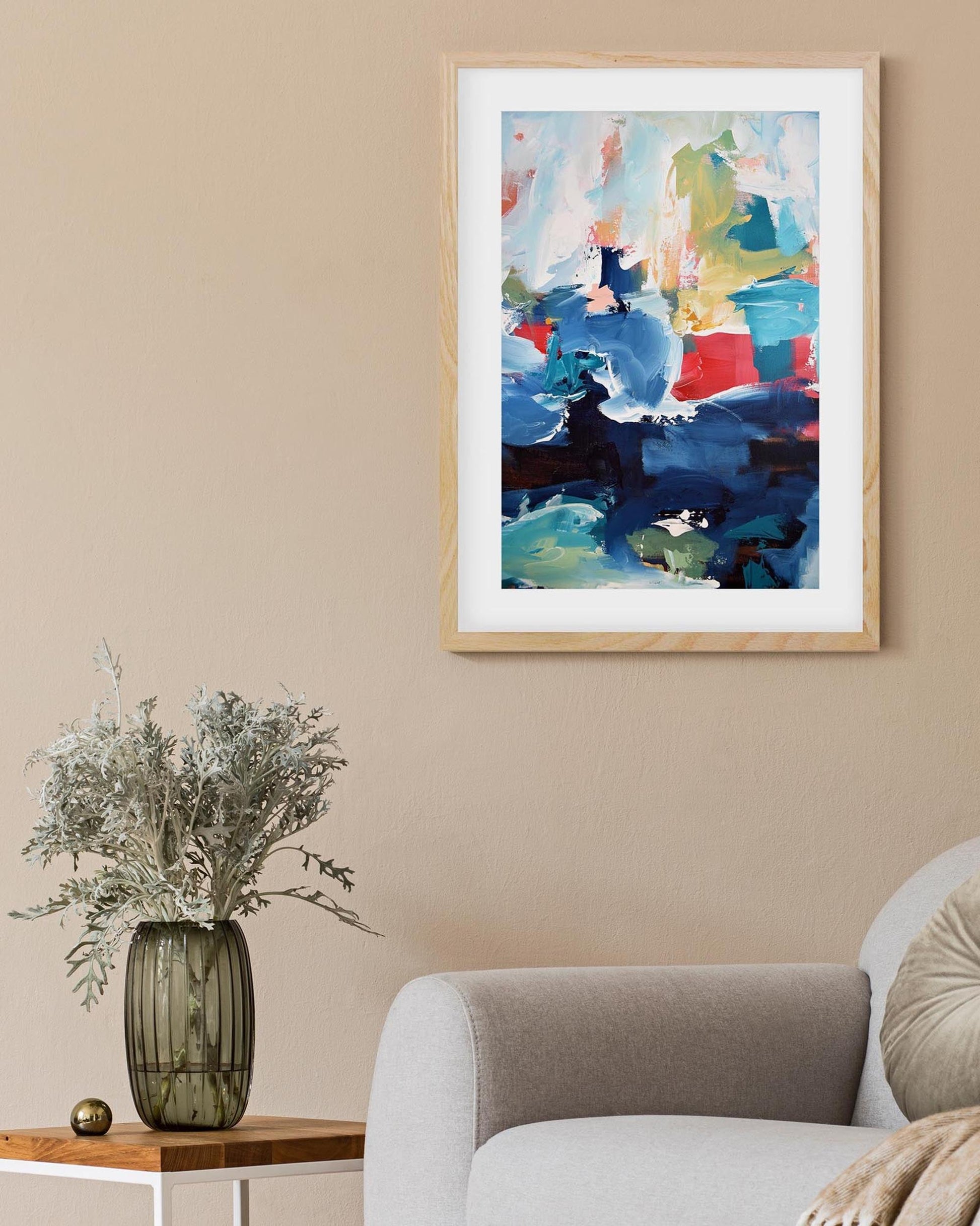 Abstract painting in a wooden frame on a beige wall above a white sofa.