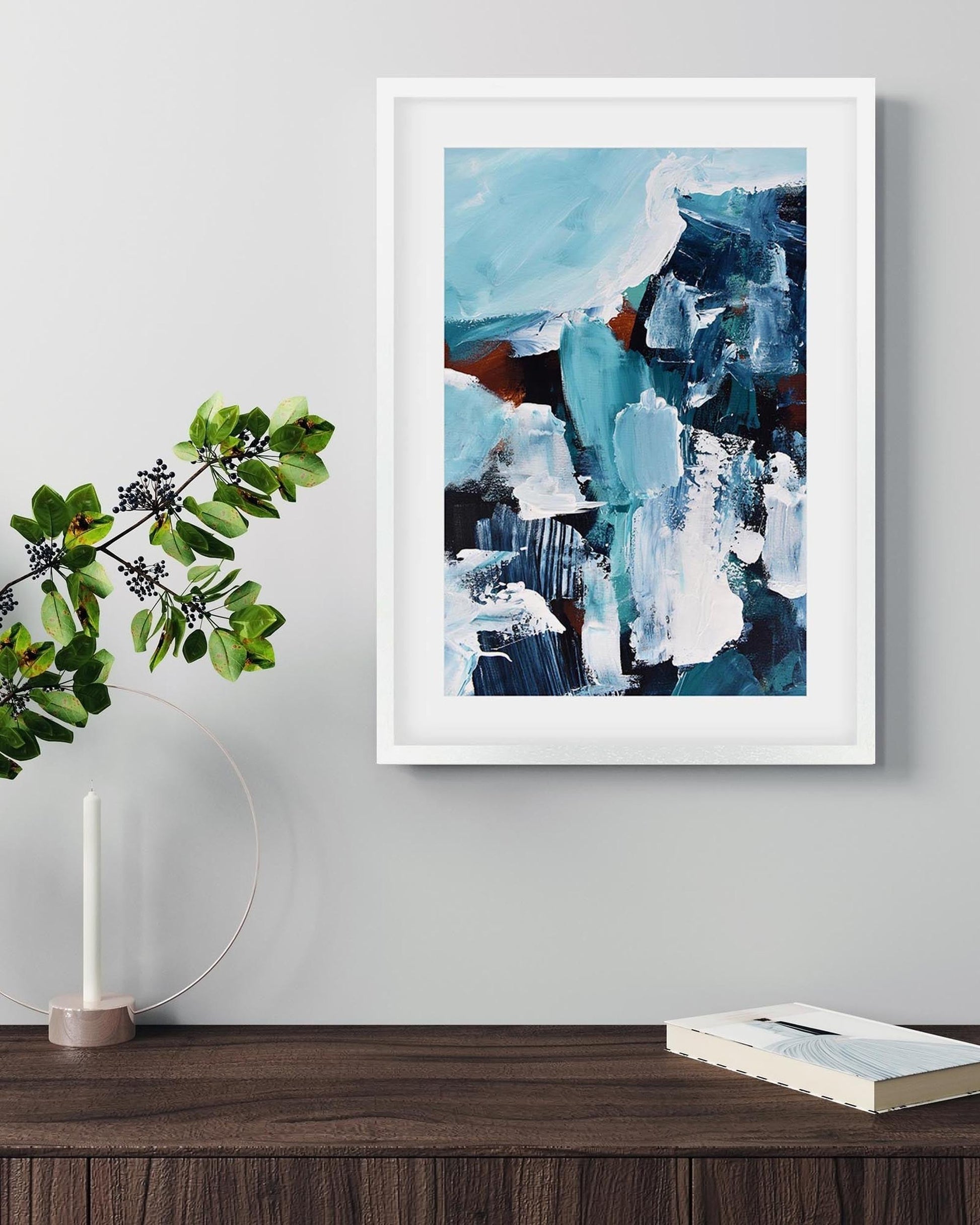 Framed abstract art piece on a wall with a plant and candle in the foreground.