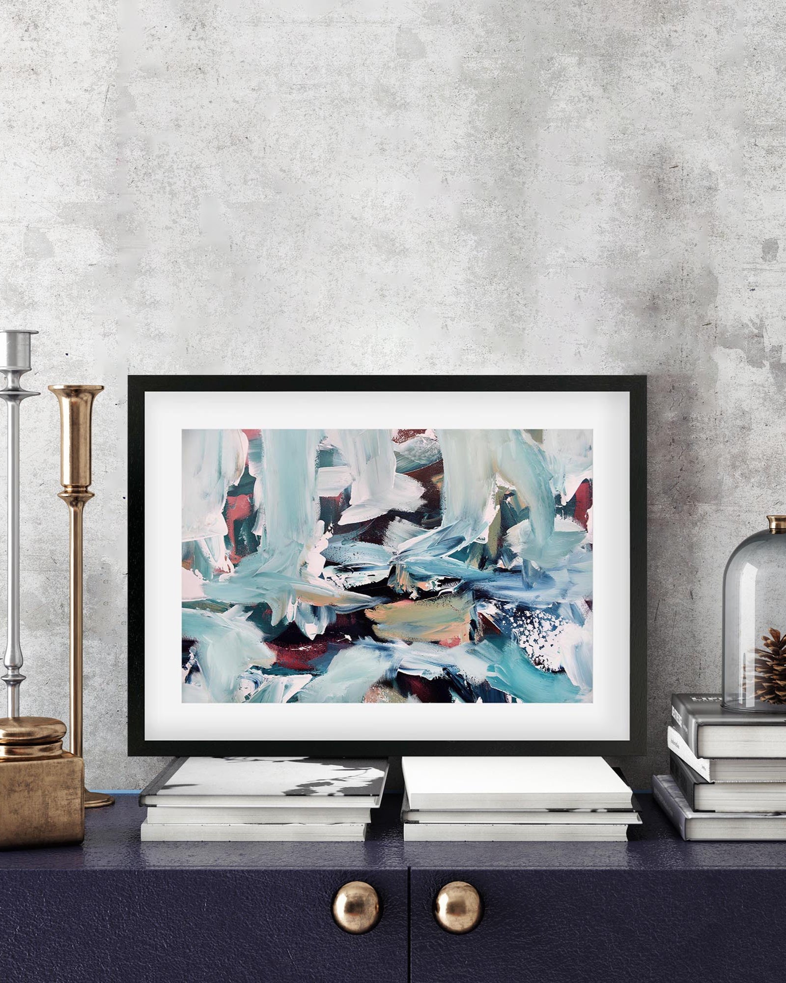 Framed abstract art piece on a shelf with decorative items against a gray wall.