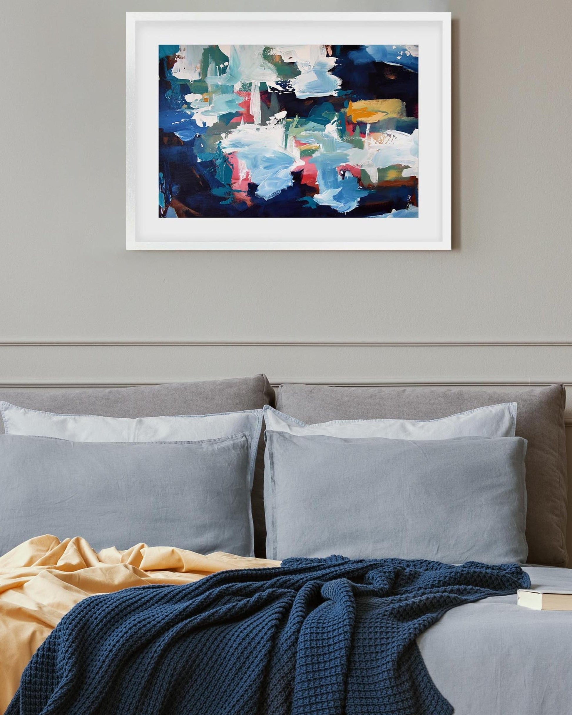 Abstract painting on a wall above a sofa with cushions and a blanket.