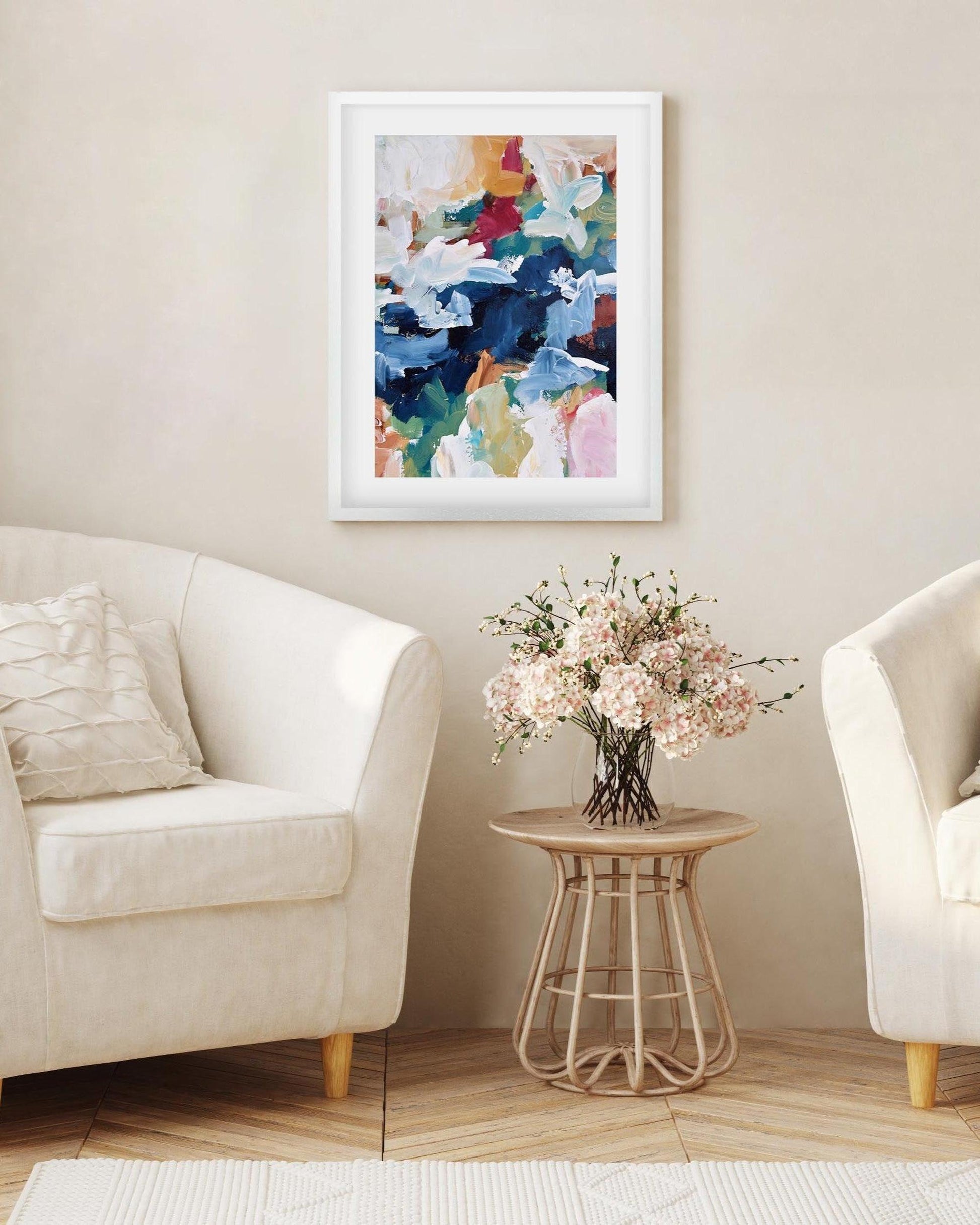 Living room with two white armchairs, a small table with flowers, and a colorful abstract painting on the wall.